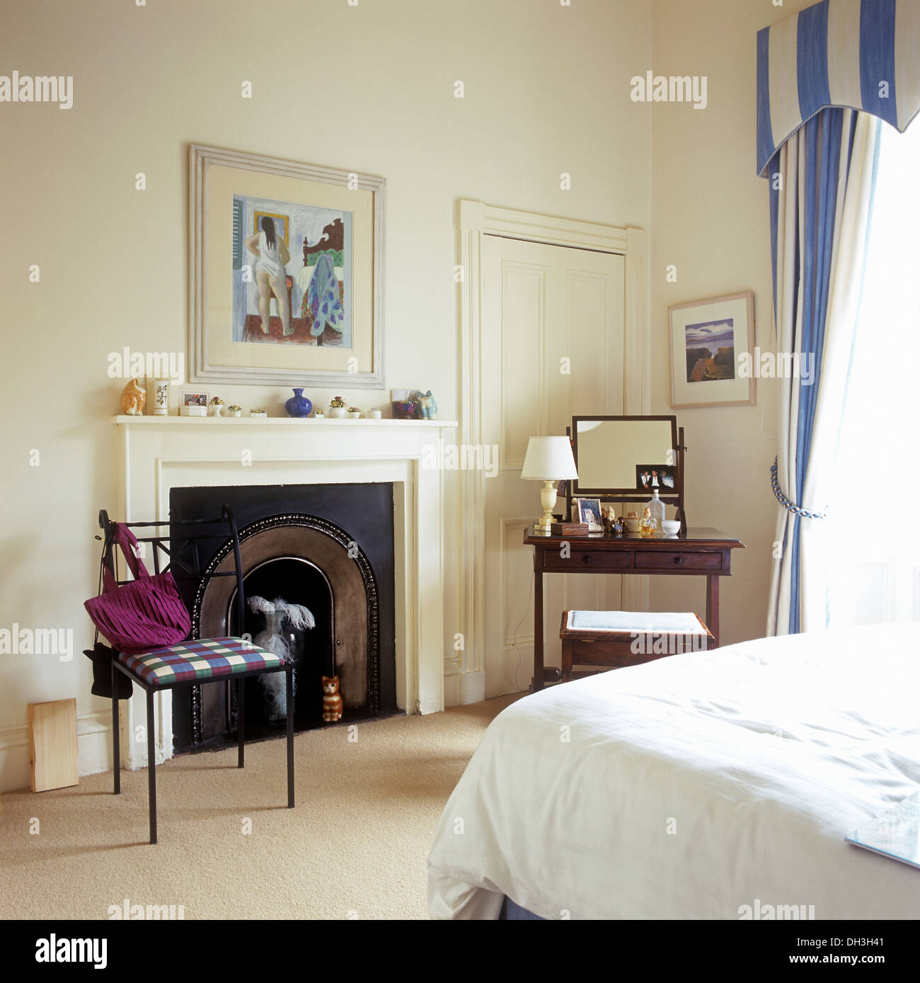 Metal chair beside fireplace in white country bedroom with blue+white curtains and cream carpet