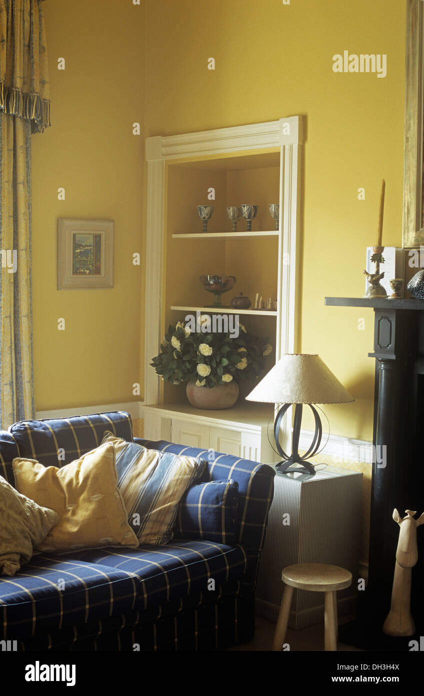 Pale yellow cushions on blue checked sofa in front of alcove shelves in