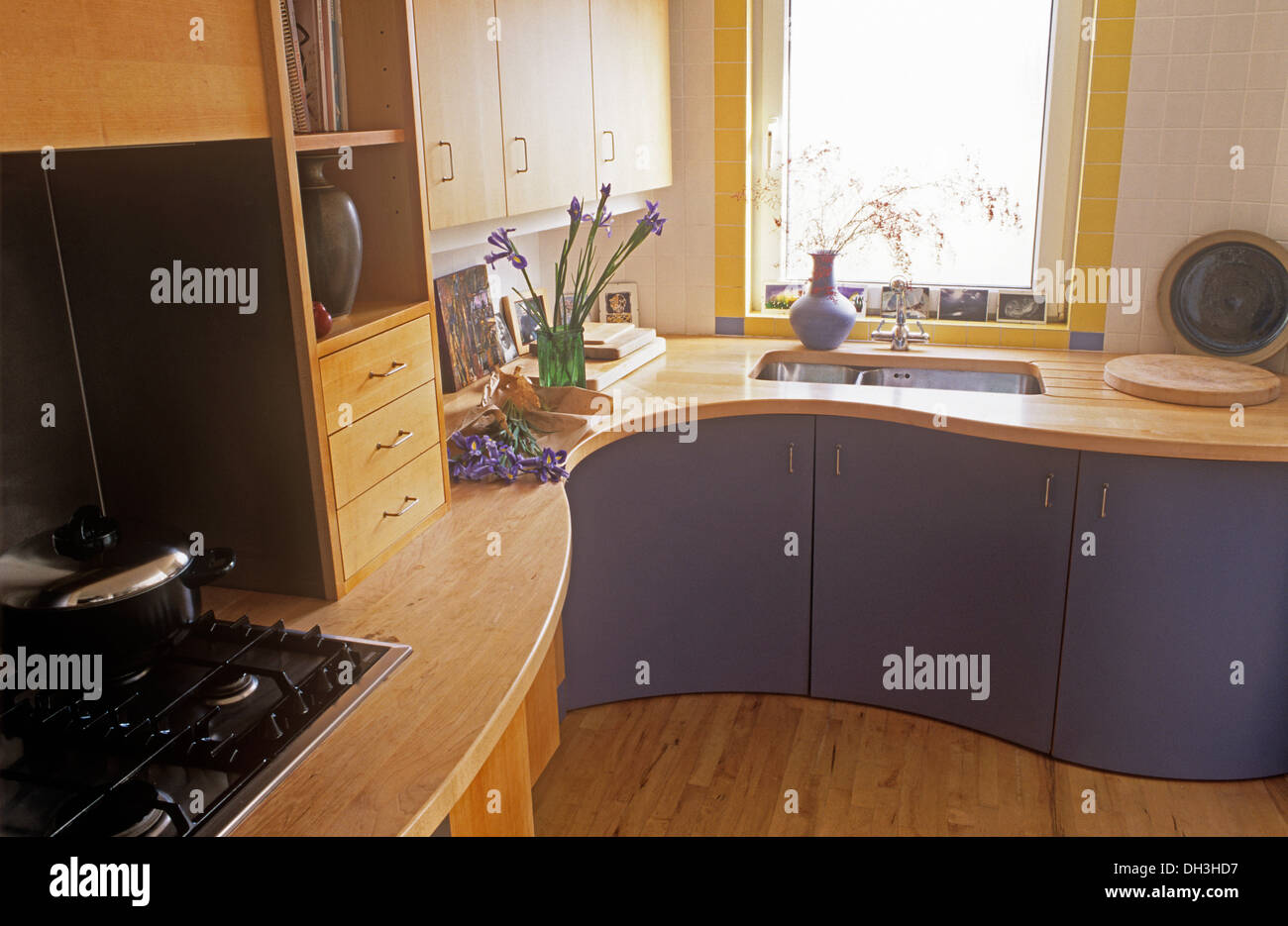 Gas hob in shaped pale wood work tops on mauve kitchen units with underset sink below window