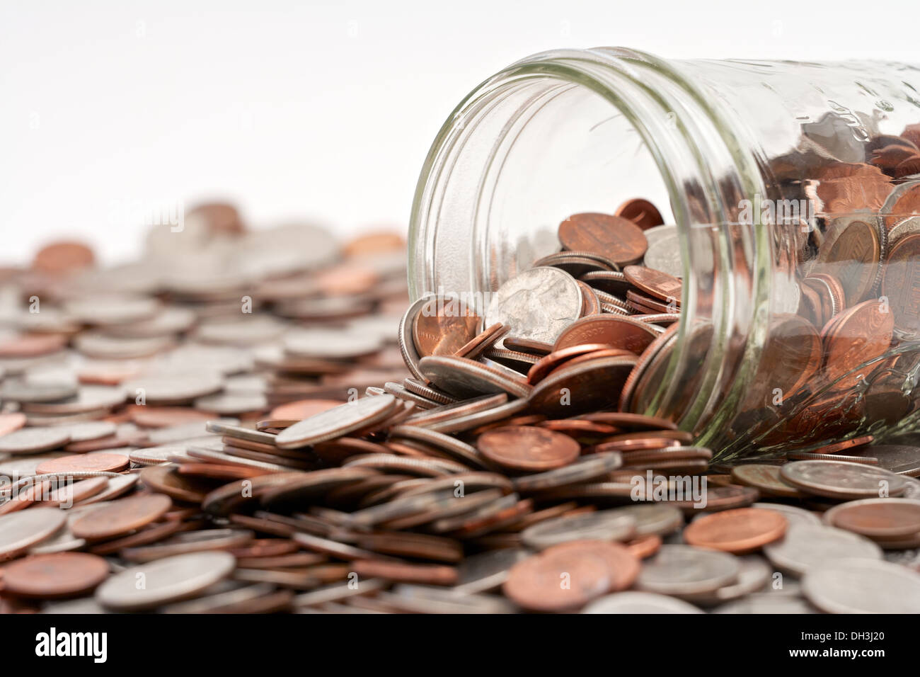 Glass mason jar full of loose pocket change spilling out on white
