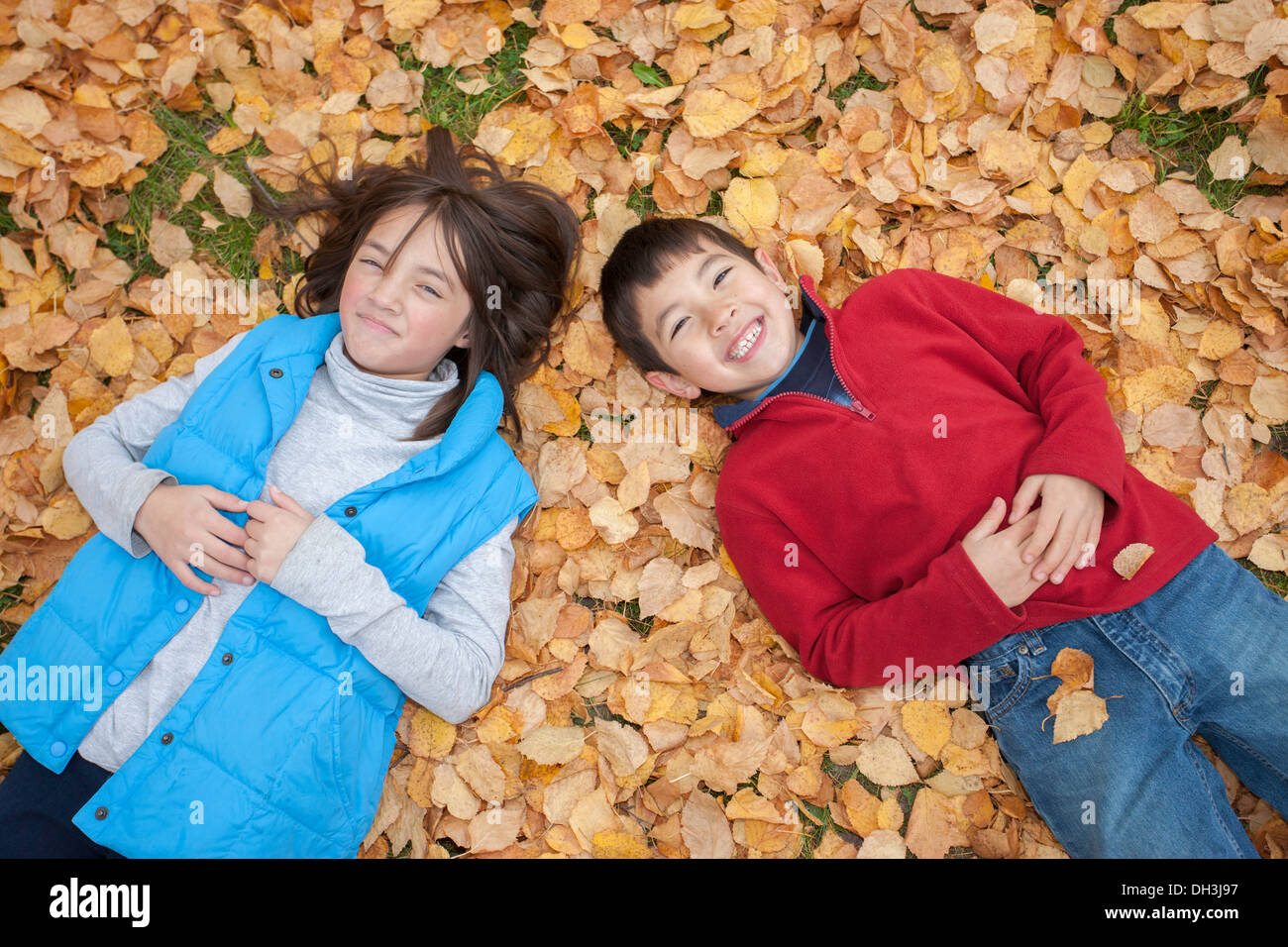 A brother and sister lay down on the ground on top of fallen leaves