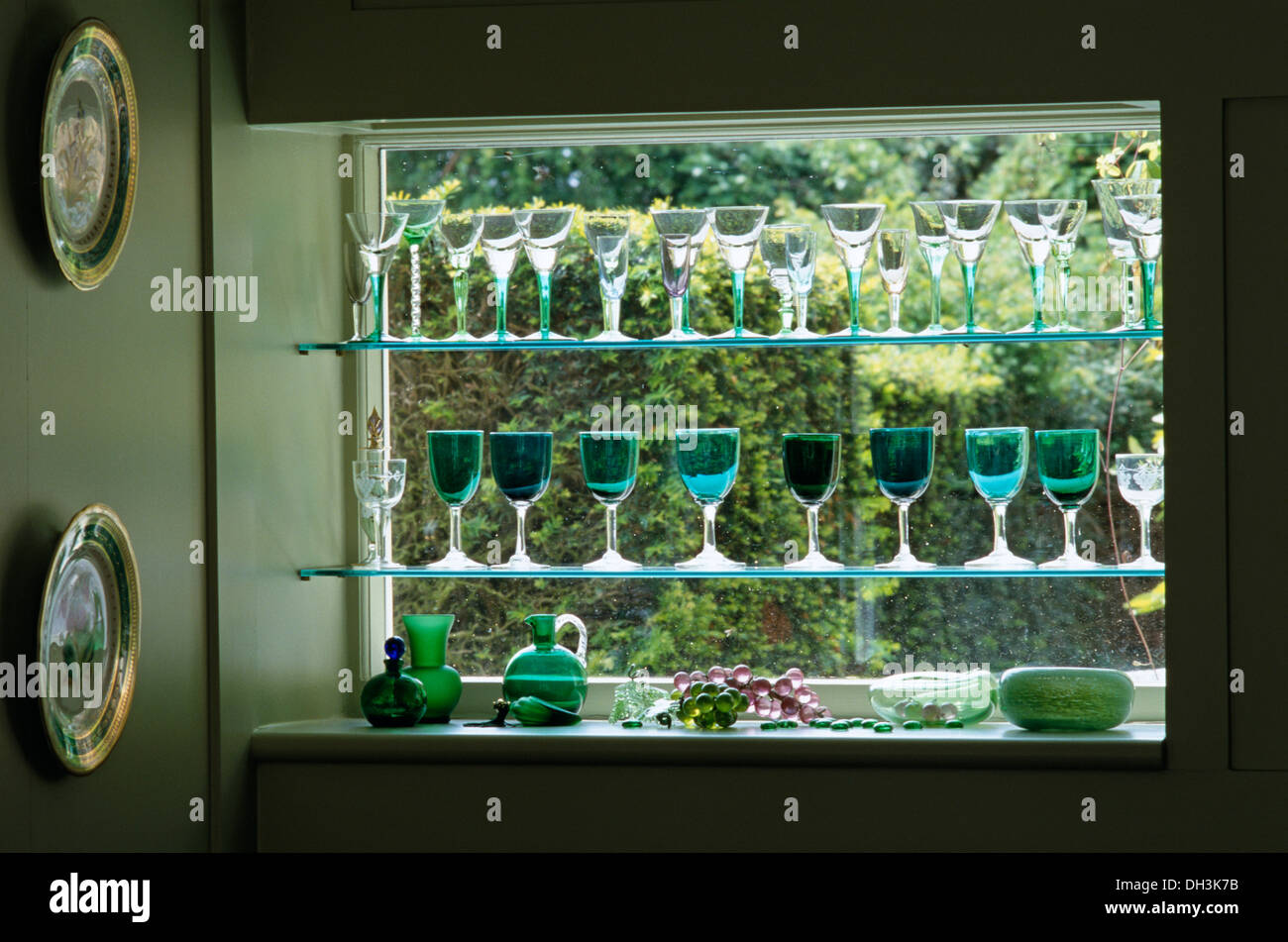 Collection of green wineglasses on glass shelves in window recess Stock