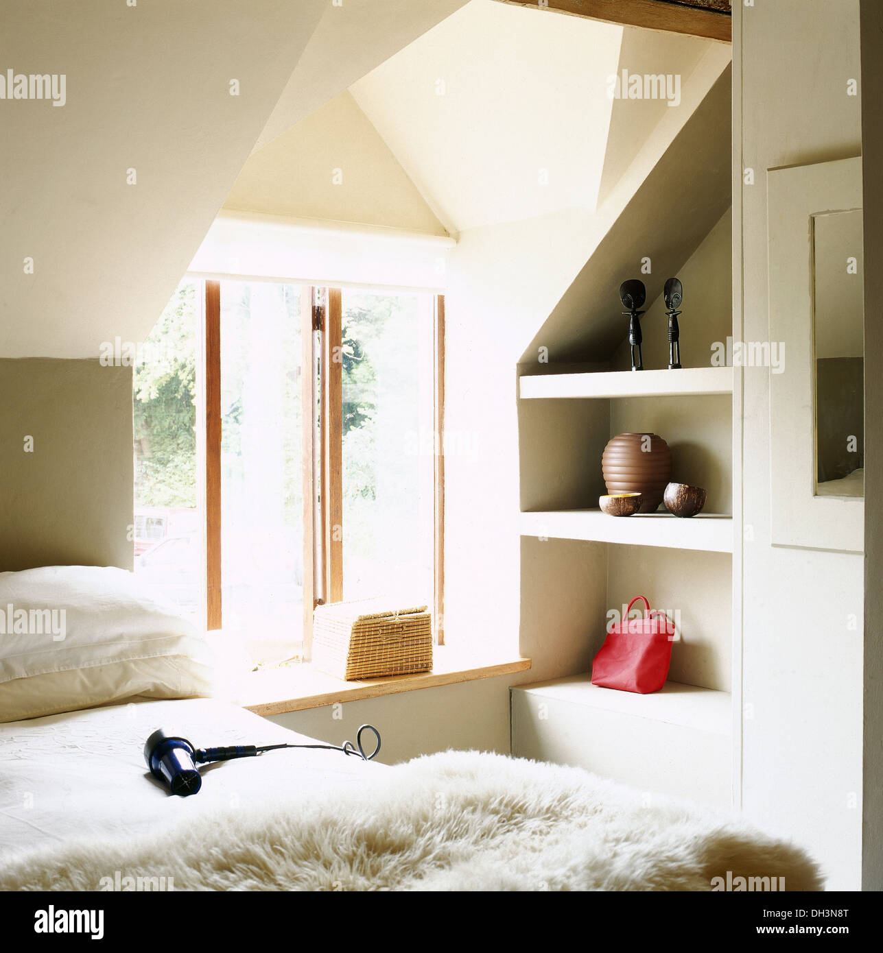Hairdryer on bed with sheepskin through in modern, loft style bedroom with open alcove shelving Stock Photo