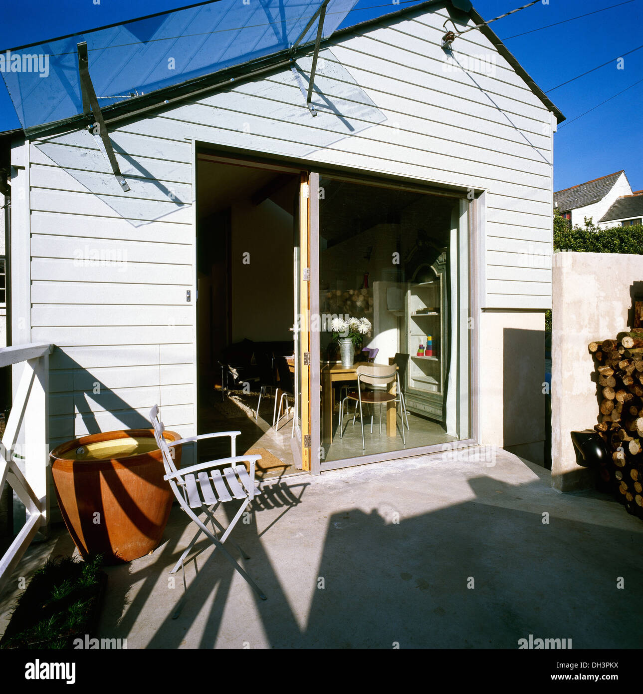 White chair on small patio in front of white painted clapboard house with sliding glass doors Stock Photo