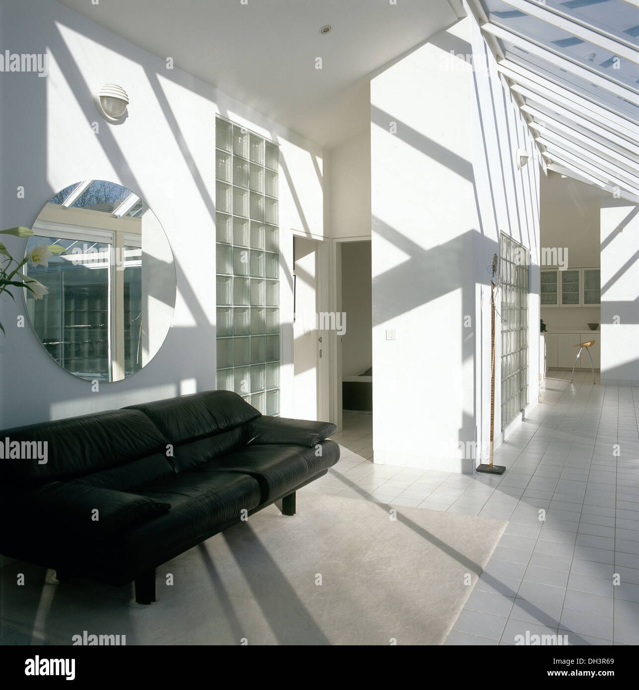 Circular Mirror Above Black Leather Sofa Next To Glass Block Wall