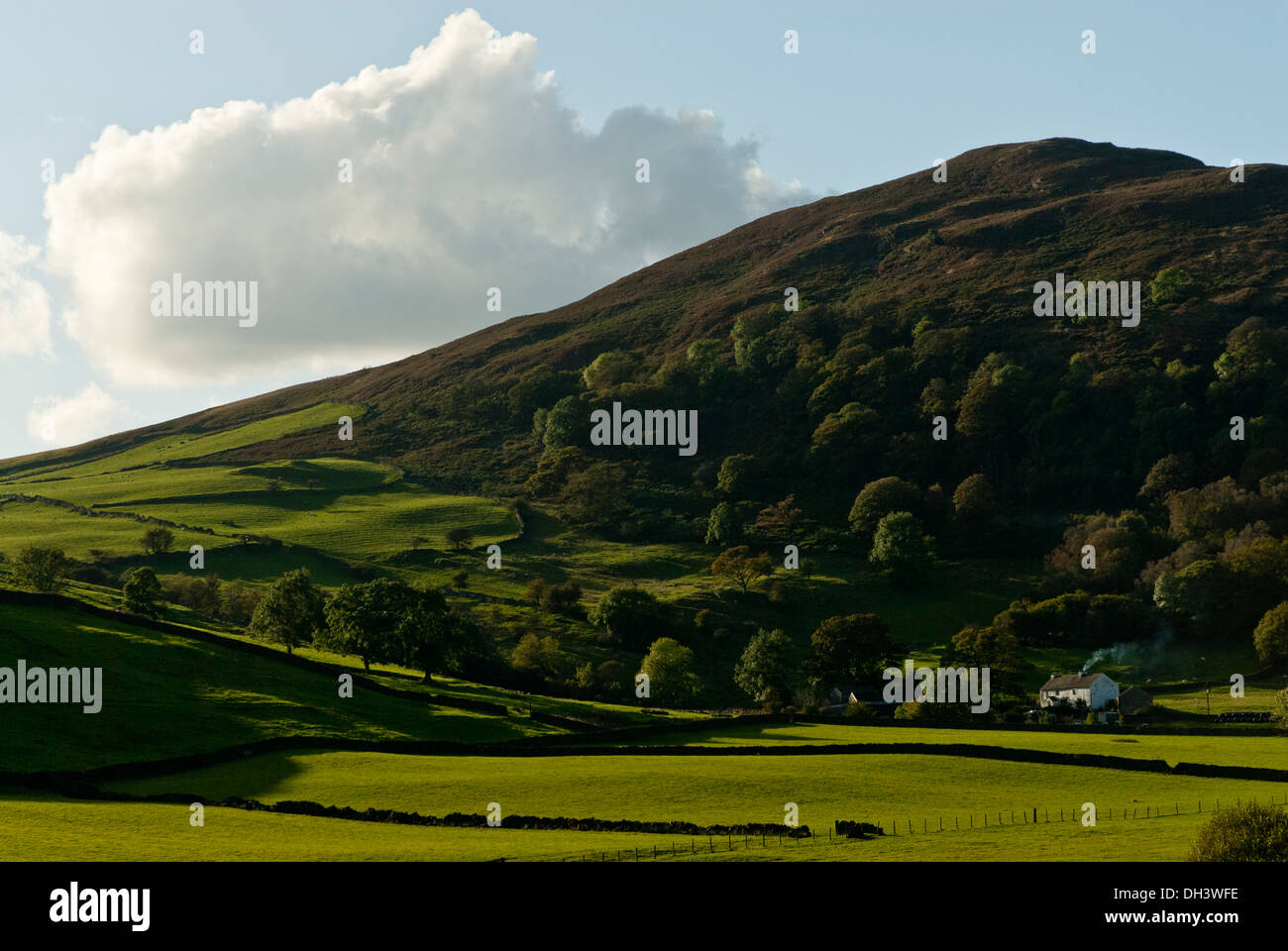 A distant farmhouse with smoking chimney in cumbria set in a a valley surrounded by hills on a bright sunny autumn day. Stock Photo