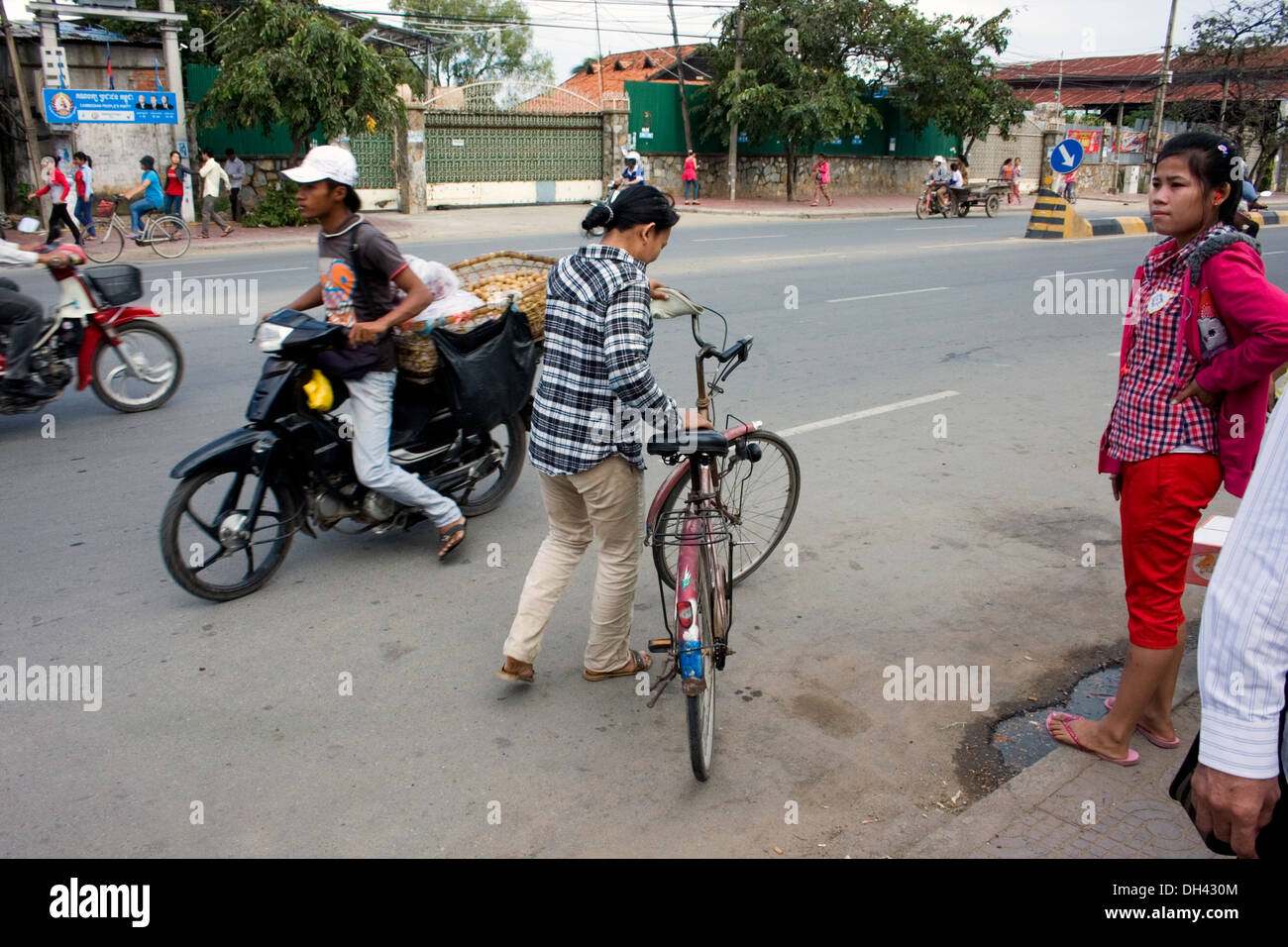 A garment factory worker is leaving a facility with her bicycle on a city street in Phnom Penh, Cambodia. Stock Photo