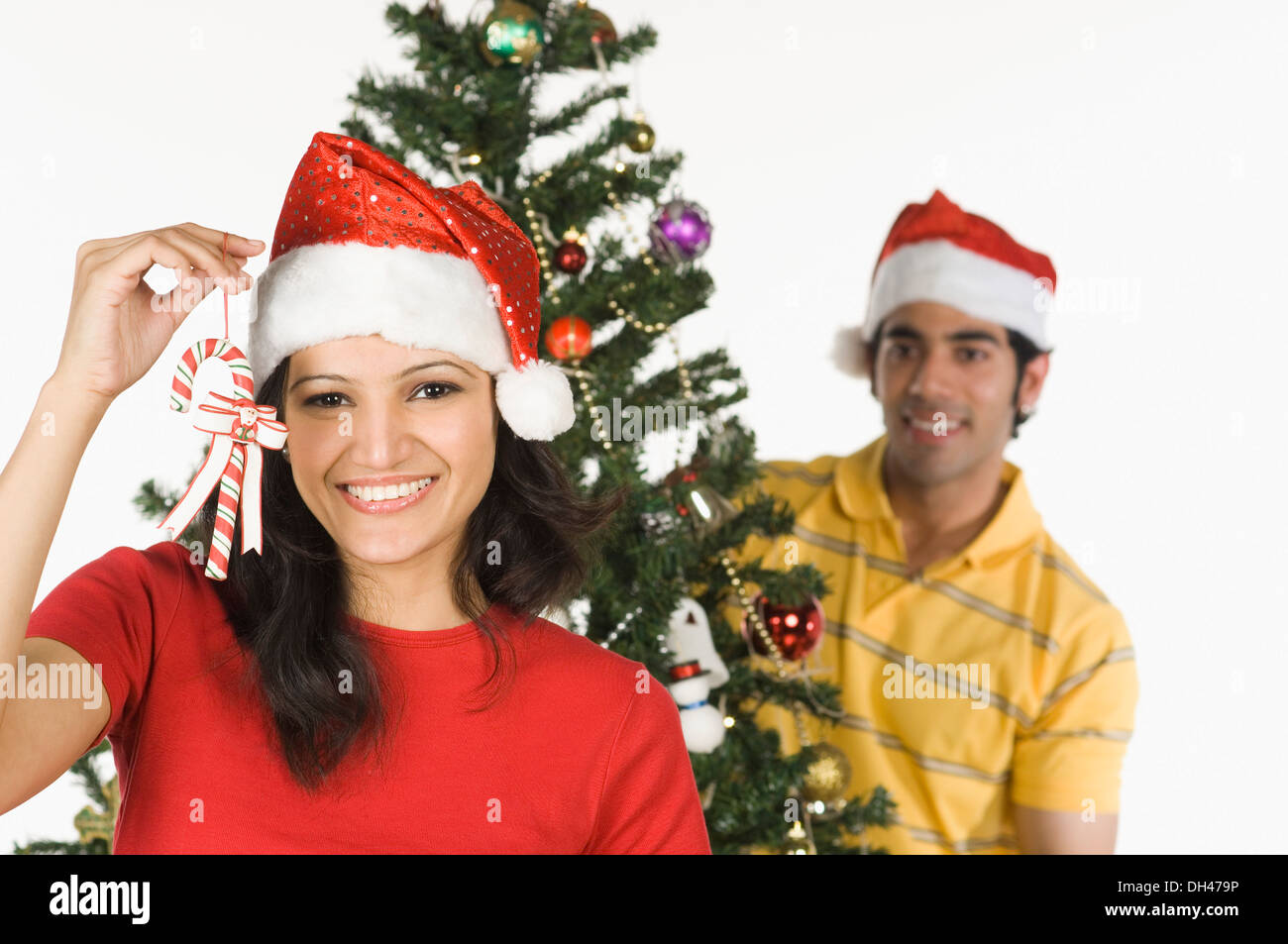 Woman showing a candy cane with a man decorating a Christmas tree in the background Stock Photo