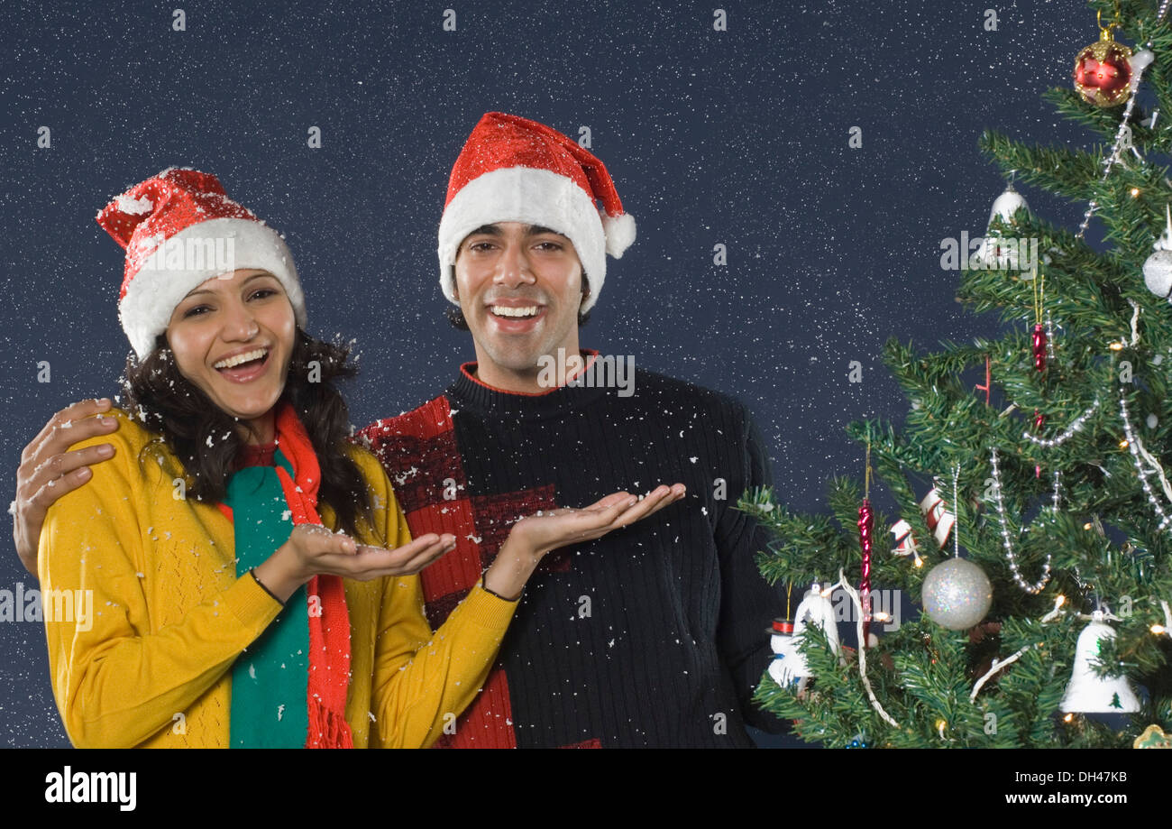 Couple standing in snow near a Christmas tree and smiling Stock Photo