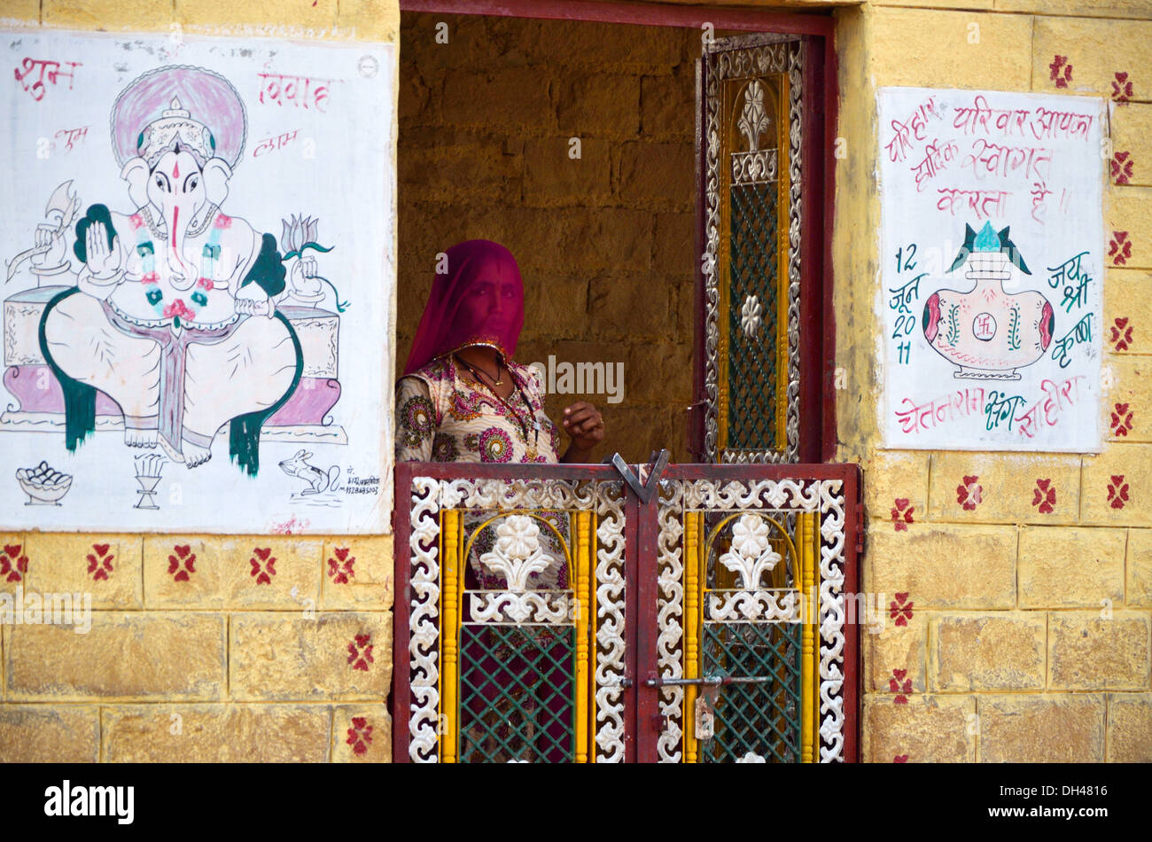 Woman in veil standing inside the gate of house with painted walls Rajasthan India Asia Stock Photo