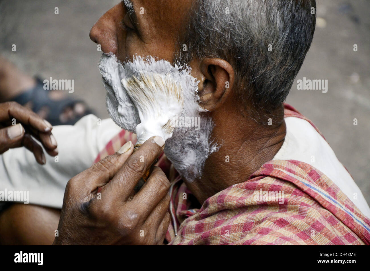 barber shaving man on roadside pavement footpath Kolkata west bengal India Stock Photo