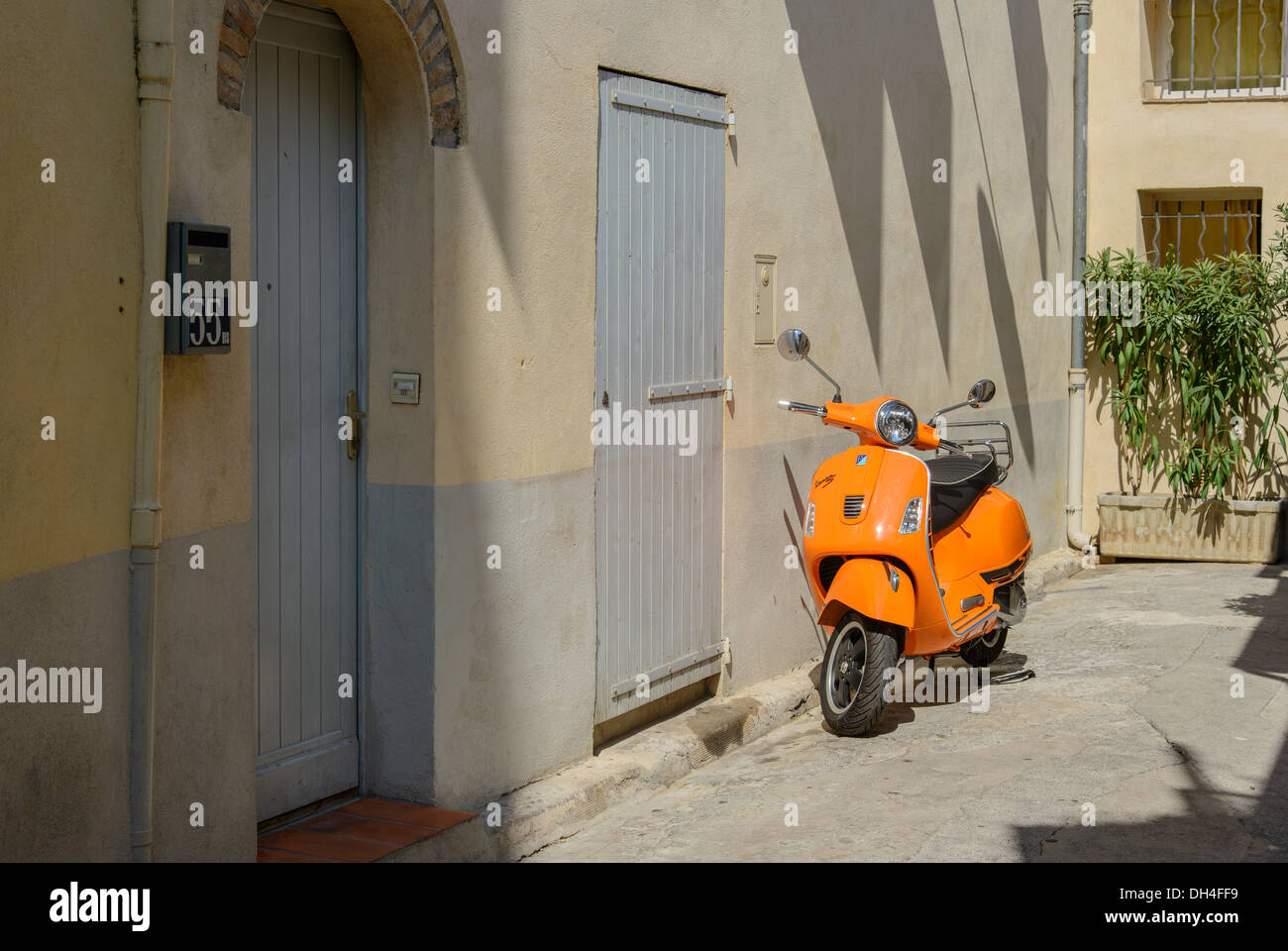 An orange motor scooter parked near a gray door in a street in Antibes