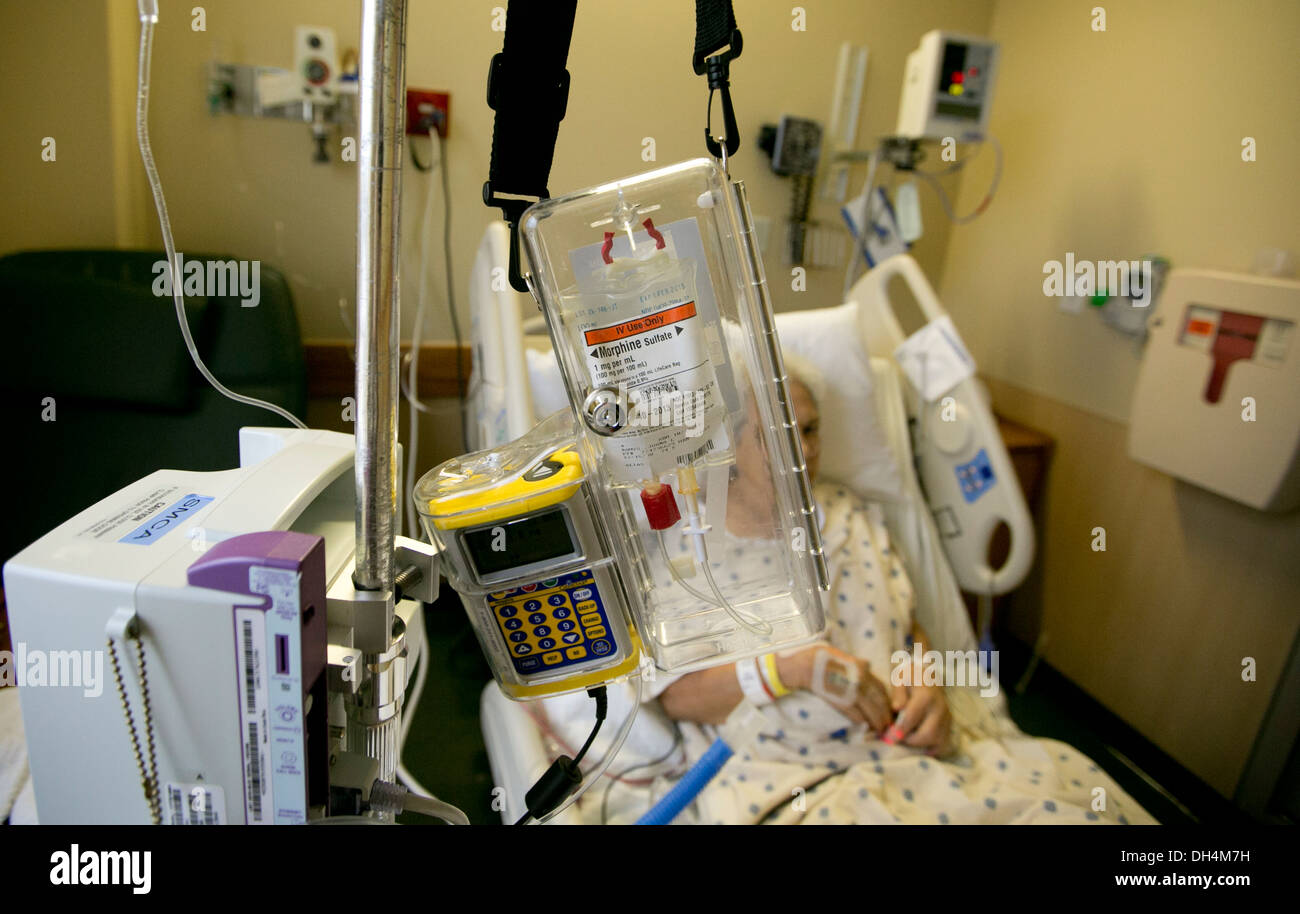 74 year old Hispanic senior woman lays in hospital bed with IV fluids and a morphine drip locked in a plastic box Stock Photo