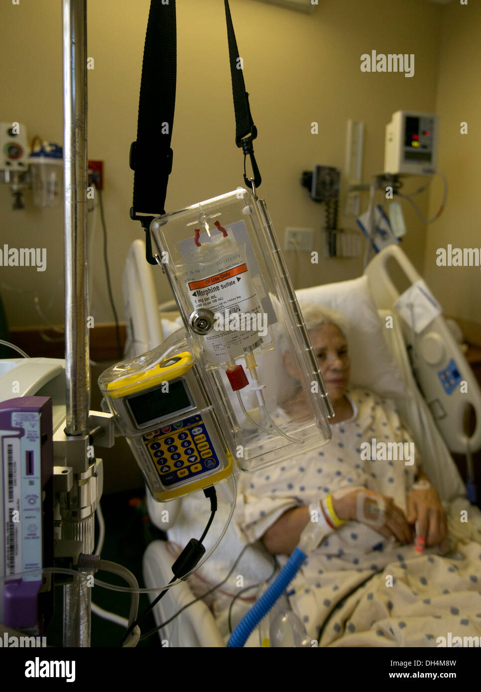 74 year old Hispanic senior woman lays in hospital bed with IV fluids and a morphine drip locked in a plastic box Stock Photo