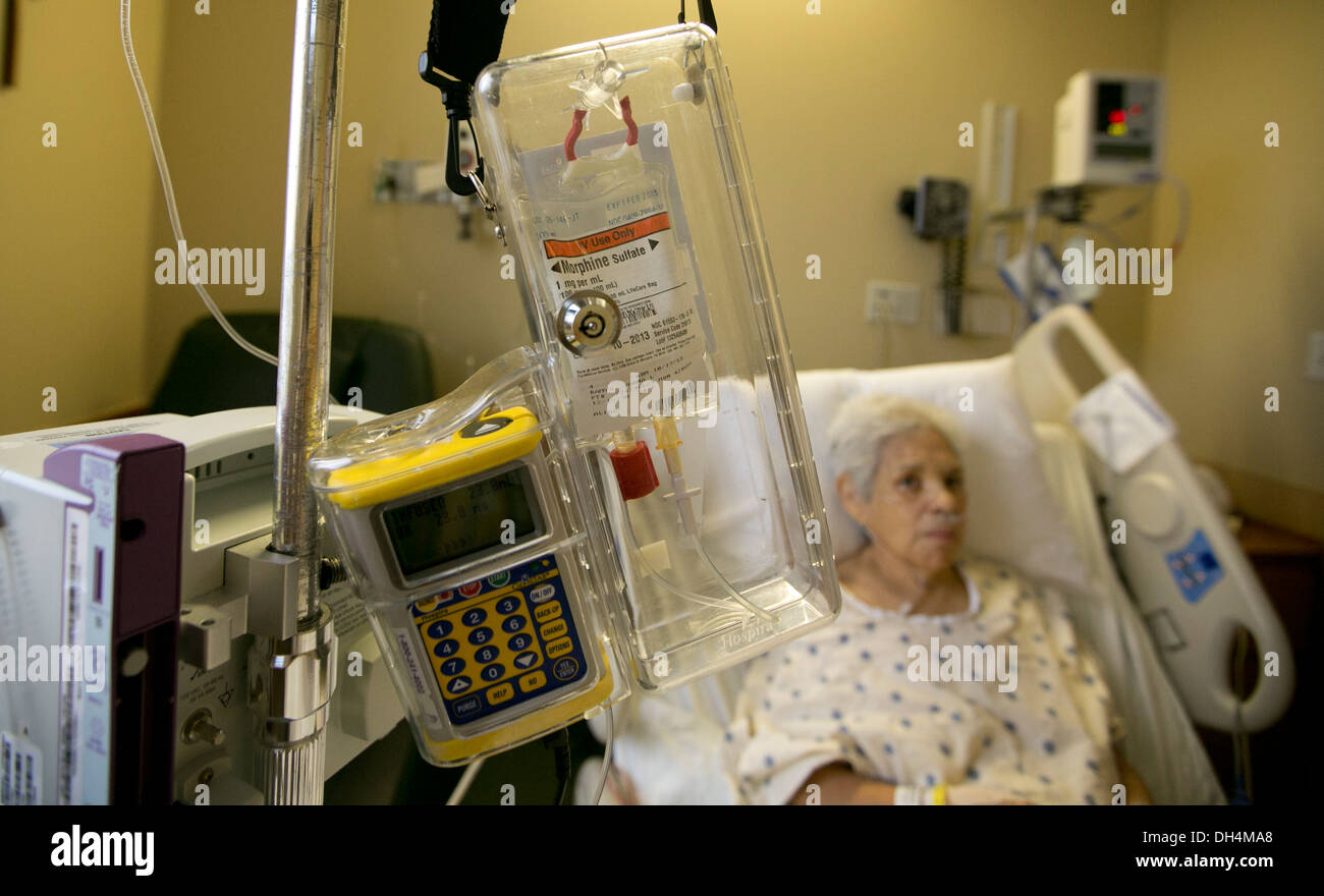 74 year old Hispanic senior woman lays in hospital bed with IV fluids and a morphine drip locked in a plastic box Stock Photo