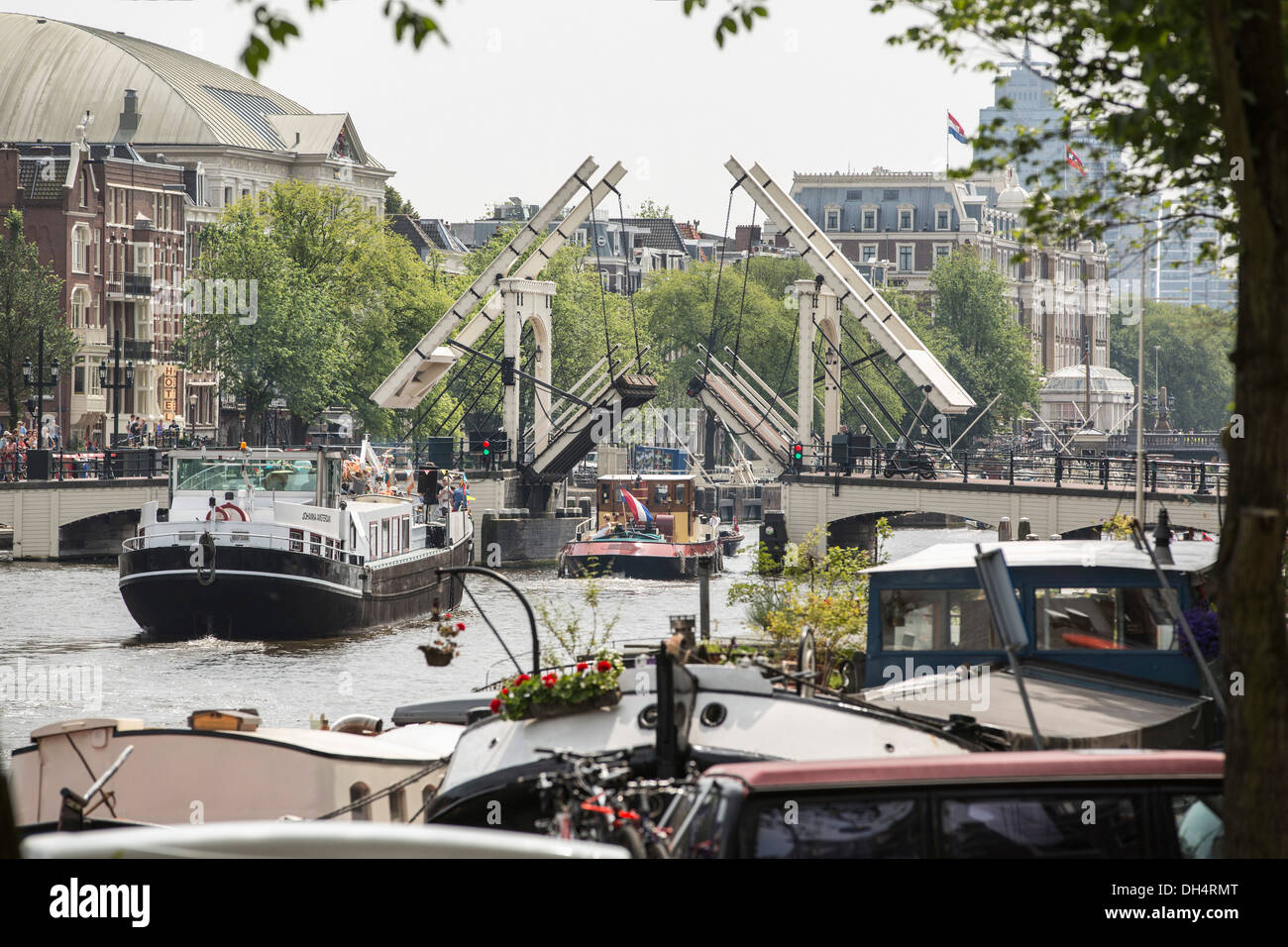 Netherlands, Amsterdam, Boats passing opened drawbridge Skinny Bridge. In front  houseboats. Back Carre theater, Amstel Hotel Stock Photo