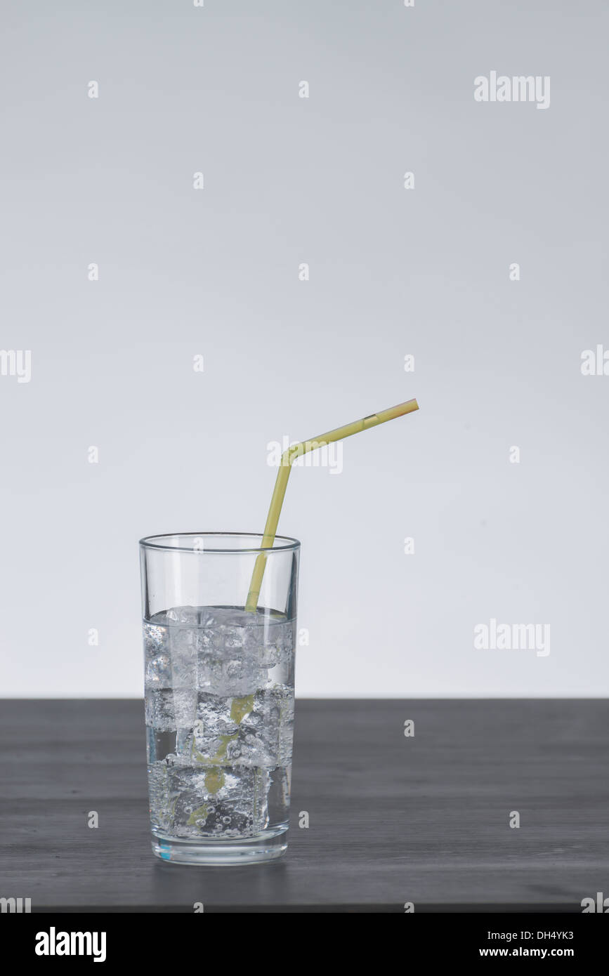 Glas with ice cubes and clear liquid drink standing on a dark brown wooden Table, yellow straw Stock Photo
