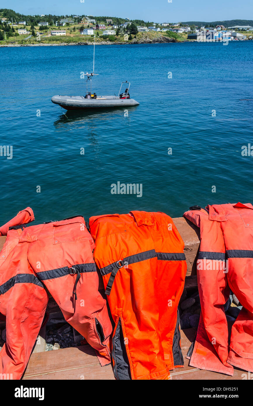 Red life preservers sit over a railing drying in the sun with a view of a dingy moored in the bay. Stock Photo