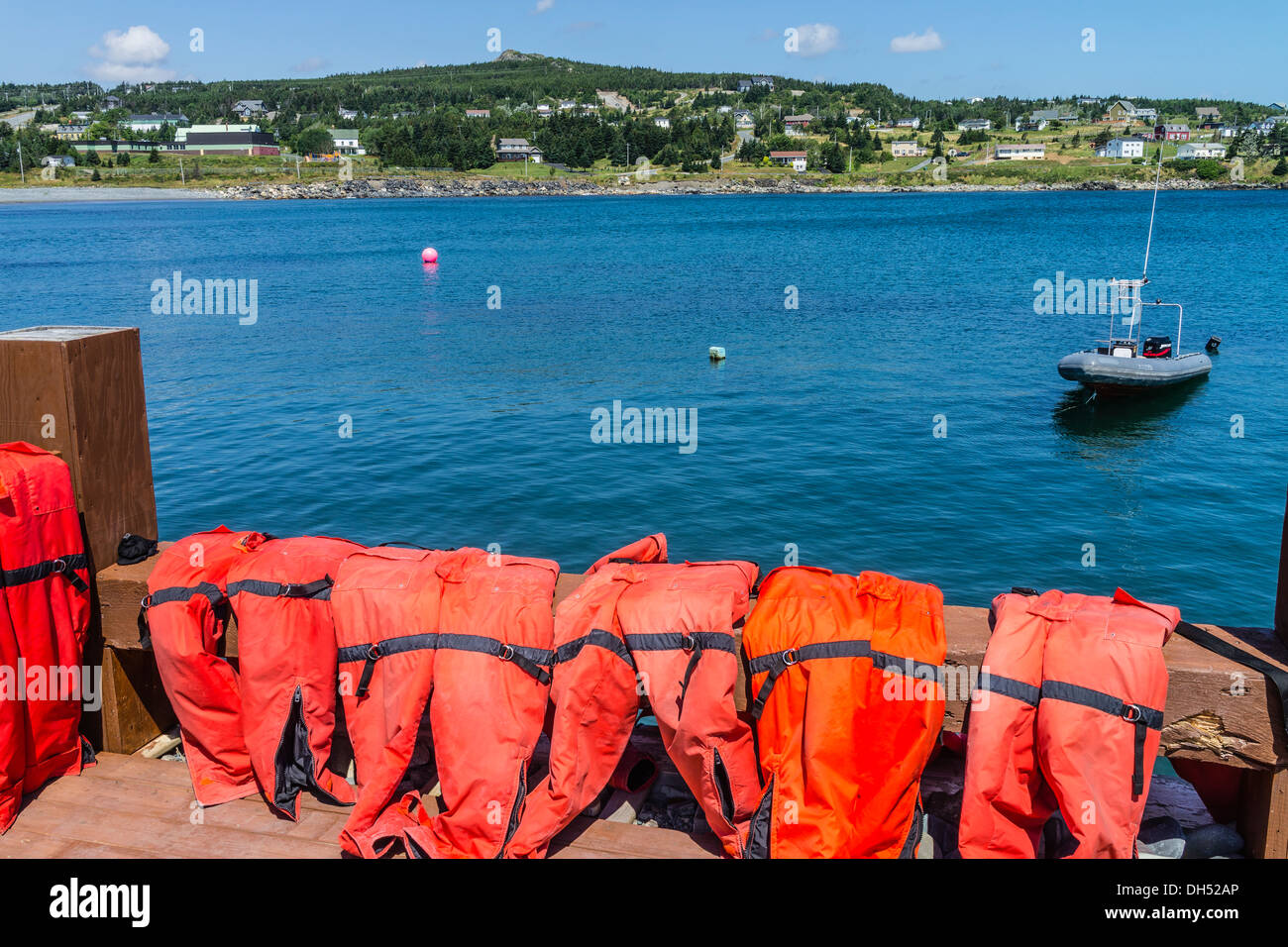 Red life preservers sit over a railing drying in the sun with a view of a dingy moored in the bay. Stock Photo