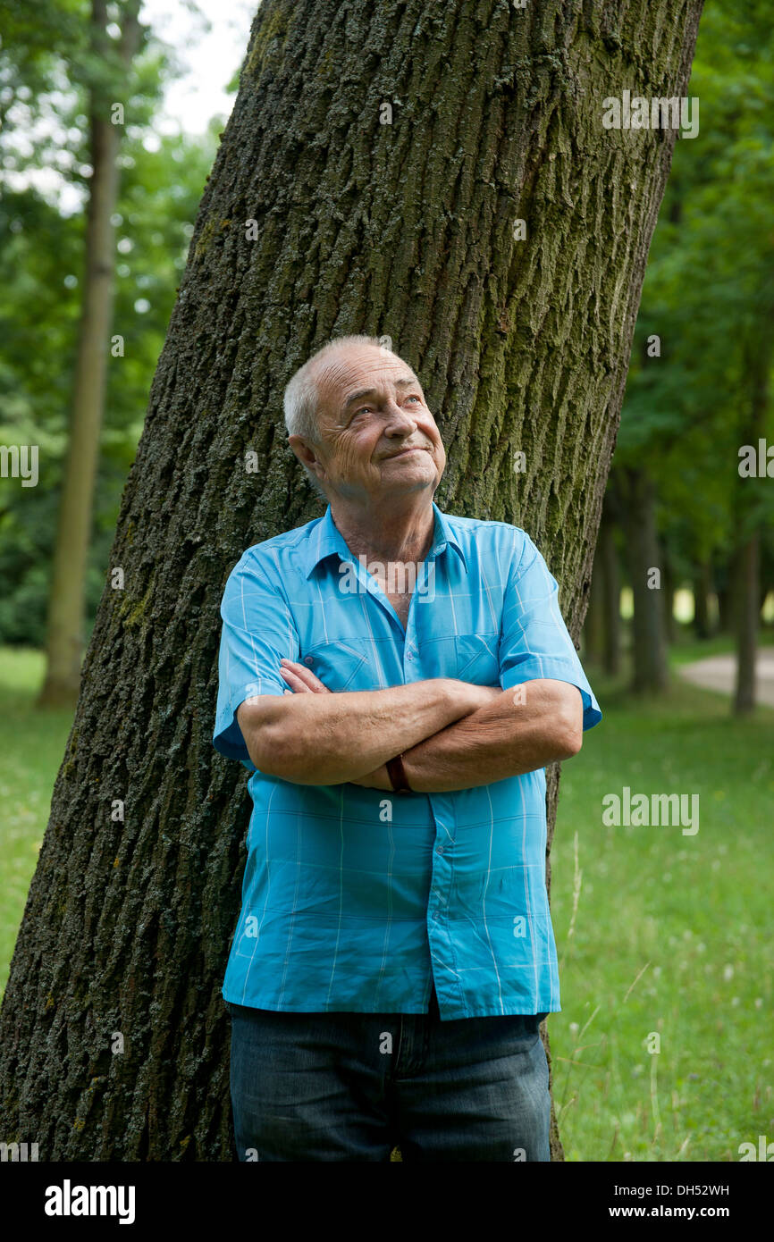 Elderly man leaning against a tree, in a good mood Stock Photo
