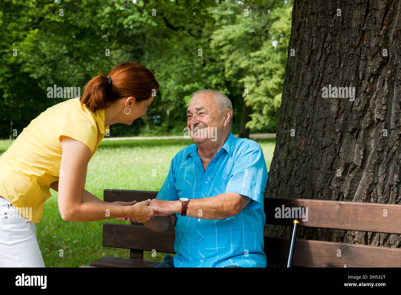Women looking after an elderly man sitting on a bench in a park Stock Photo