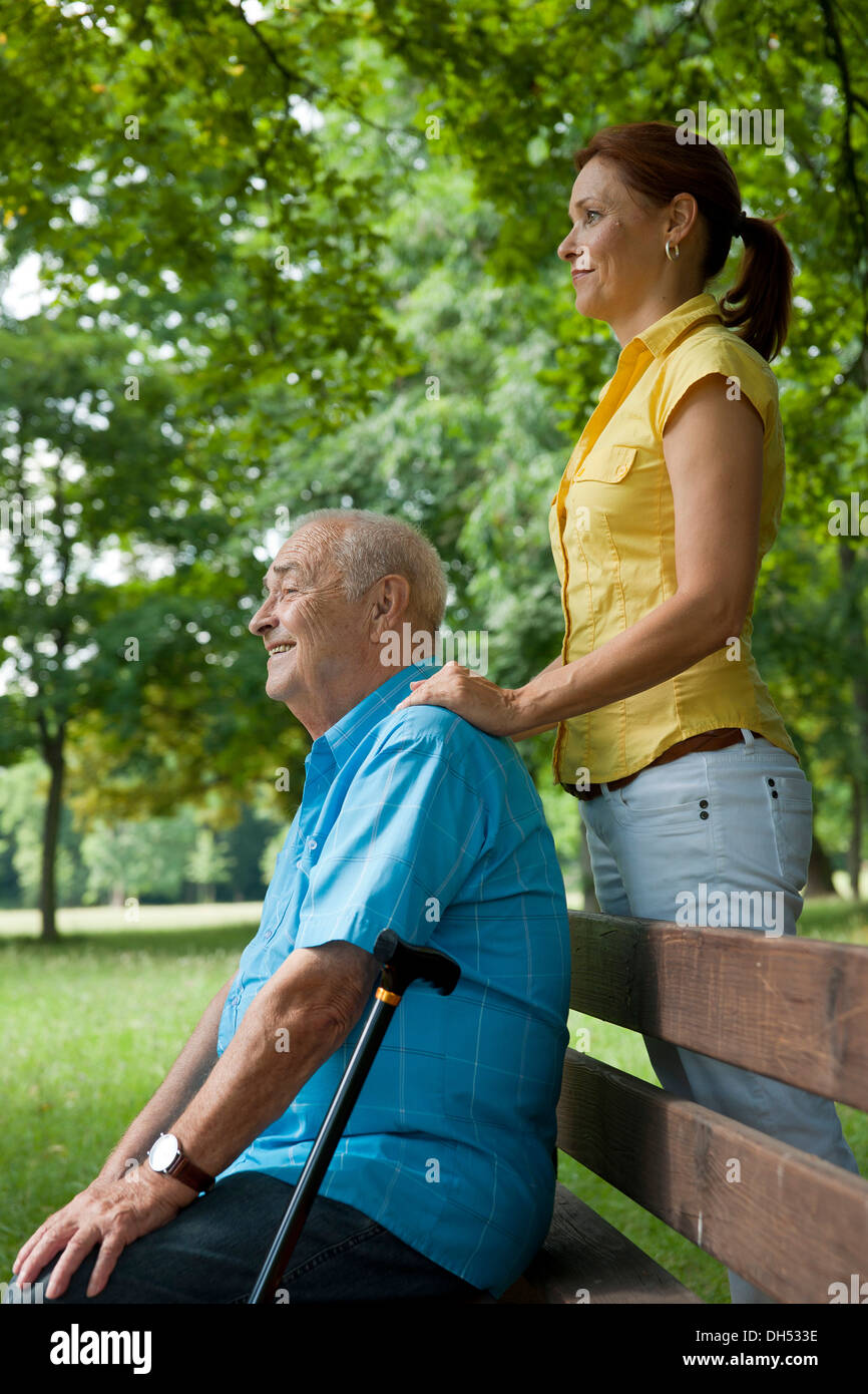 Women looking after an elderly man sitting on a bench in a park Stock Photo