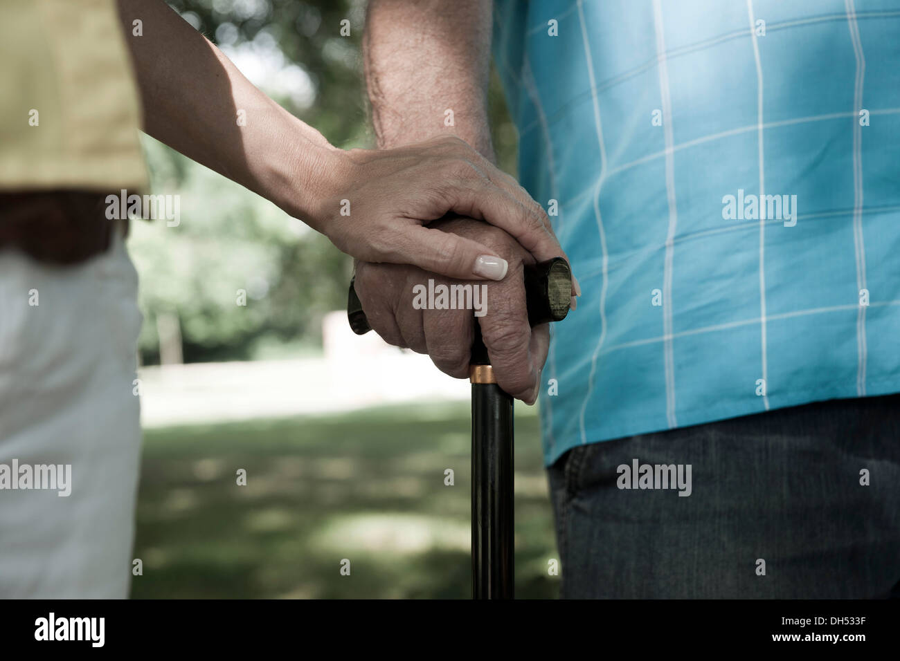 Woman putting her hand on the hand of an elderly man holding a walking stick Stock Photo