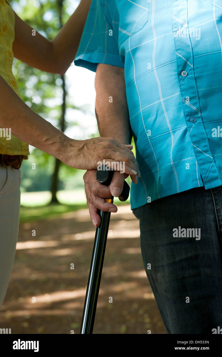 Woman putting her hand on the hand of an elderly man holding a walking stick Stock Photo