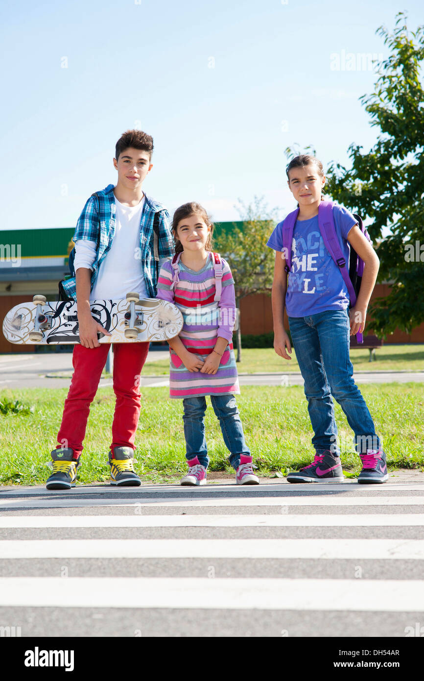 Children with a skateboard and carrying school bags on the way to school Stock Photo