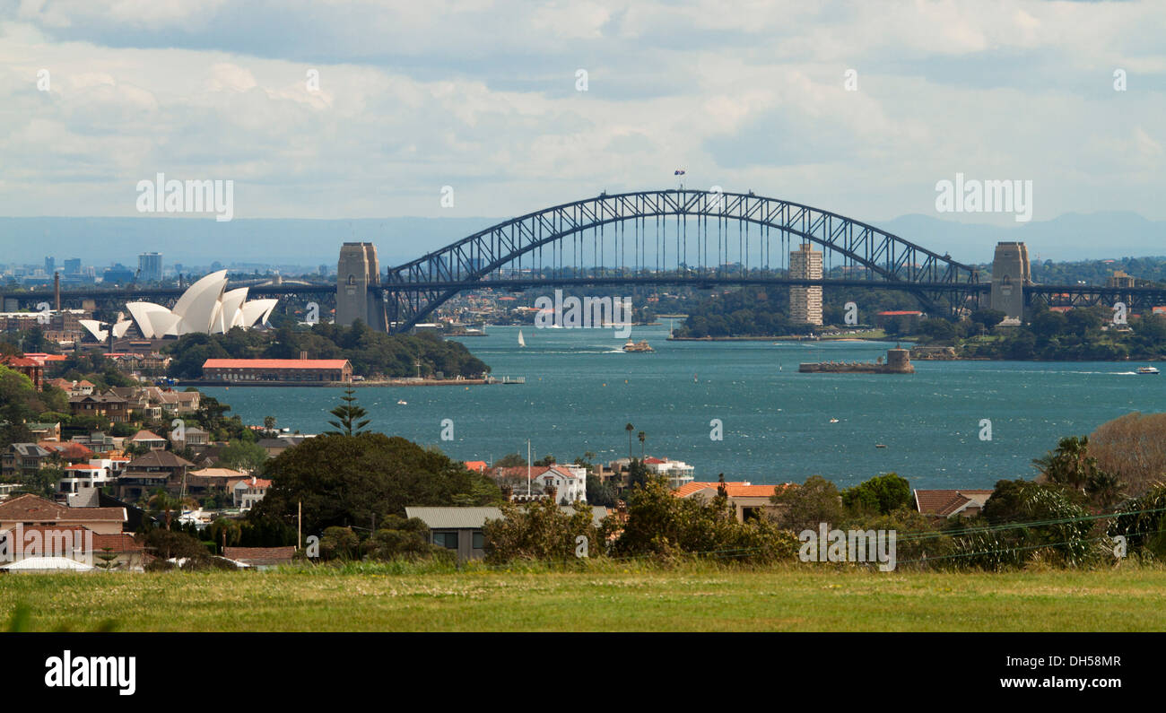 Panoramic city landscape showing Sydney harbour bridge, iconic opera house, and houses beside blue waters of Darling Harbour Stock Photo