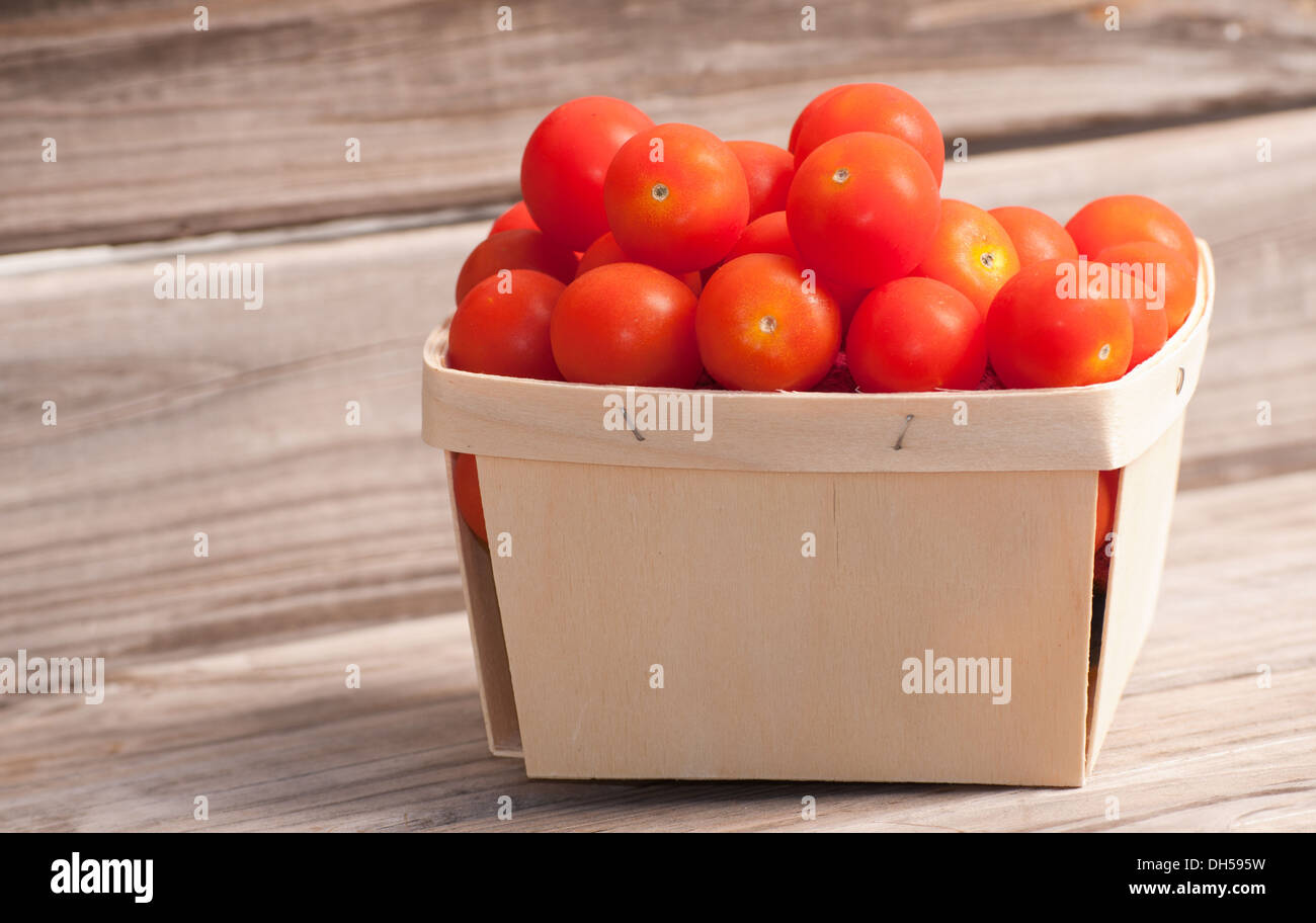 Small woven basket with ripe cherry tomatoes; on rustic wood board background Stock Photo