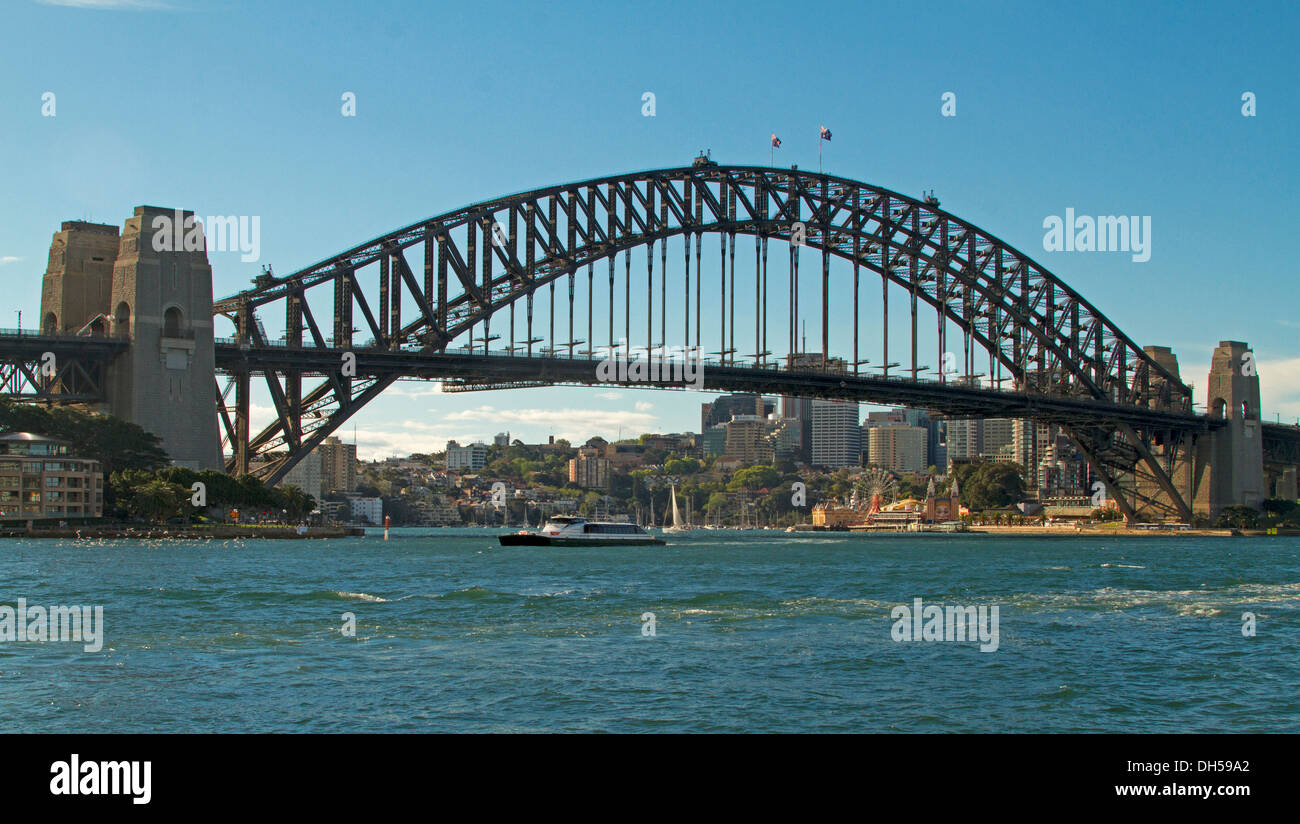 Panoramic view of Sydney harbour bridge spanning blue waters with commuter ferry passing beneath this iconic structure in NSW Australia Stock Photo
