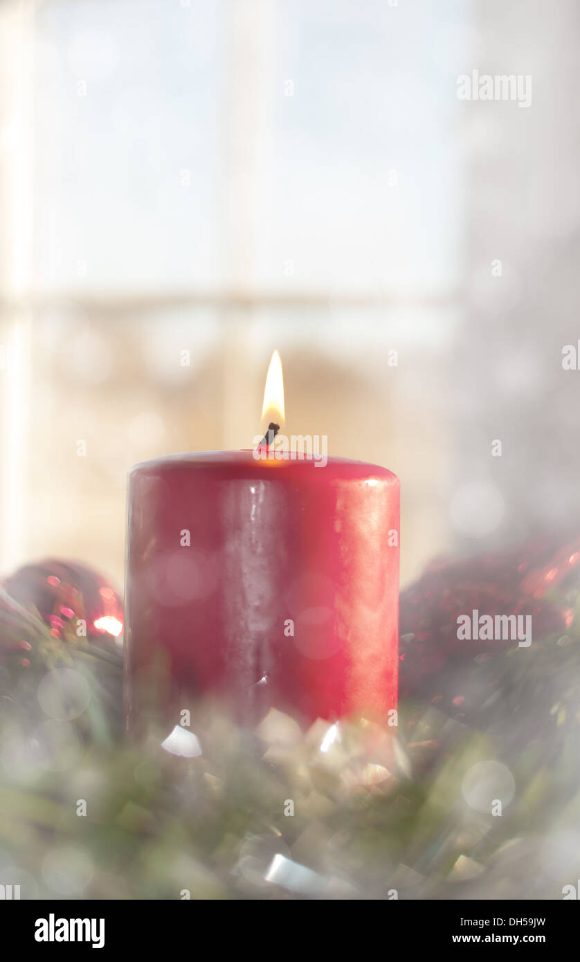 Dreamy image of a Red Christmas candle burning inside a wreath, with a window on background Stock Photo