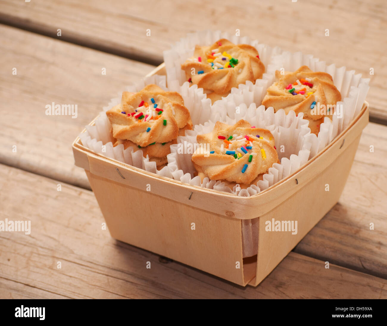 Cookies with colorful sprinkles on top, in a woven wooden basket on rustic board background Stock Photo