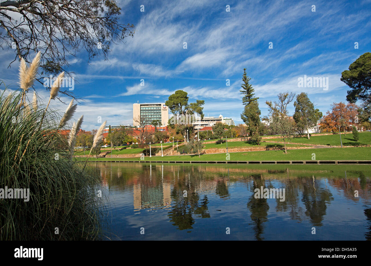 Urban landscape of parklands and Torrens River / Lake in Adelaide with city buildings and trees reflected in calm blue water Stock Photo