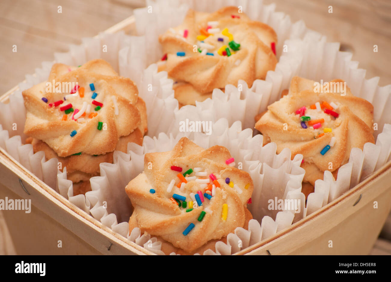 Closeup of shortbread cookies with colorful nonpareil sprinkles on top, in a wooden basket Stock Photo