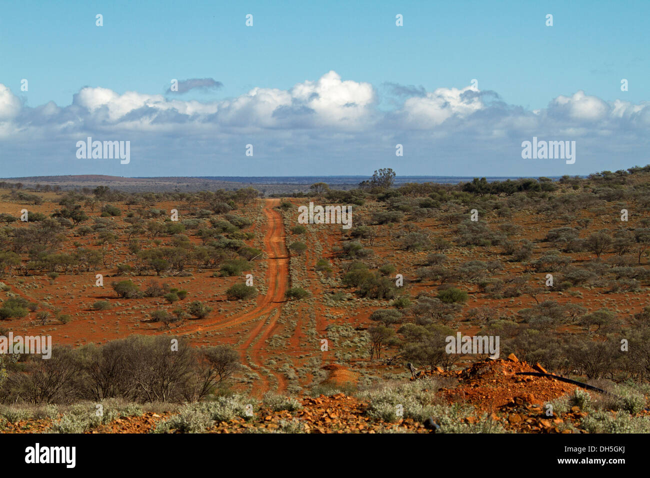 View of vast outback landscape with red road leading across plains with low vegetation from hill to distant horizon and blue sky in South Australia Stock Photo
