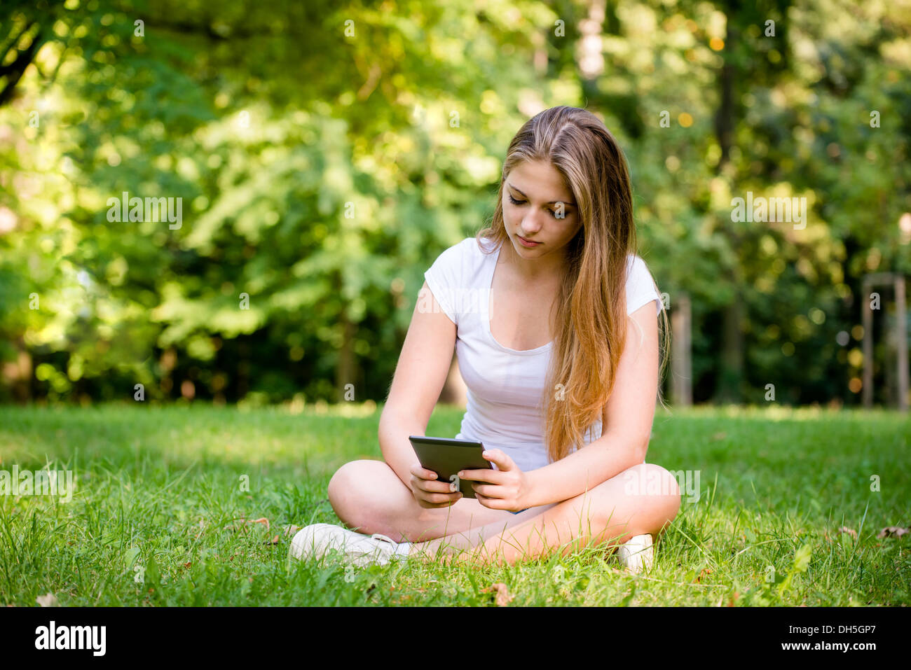 Young woman (teen girl) reading book on electronic book reader - outdoor in nature Stock Photo