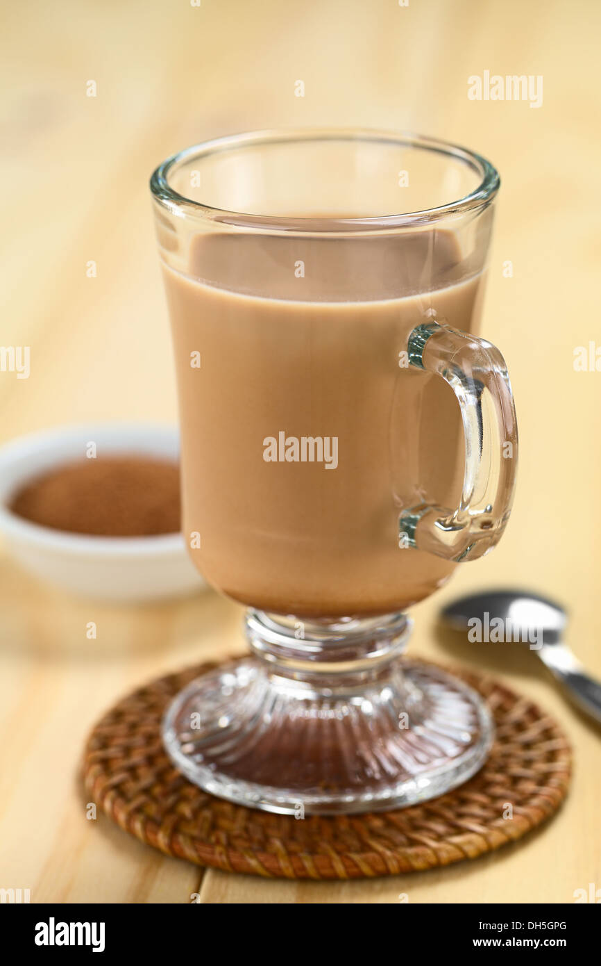 Hot chocolate with cocoa powder and spoon in the back (Selective Focus, Focus on the front rim of the glass) Stock Photo