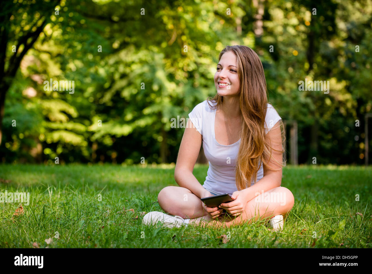 Young woman (teen girl) reading book on electronic book reader - outdoor in nature Stock Photo