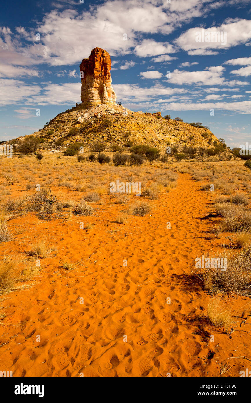 Stark Australian outback landscape - immense red rocky column Chambers Pillar spearing into blue sky with tufts of white clouds Stock Photo