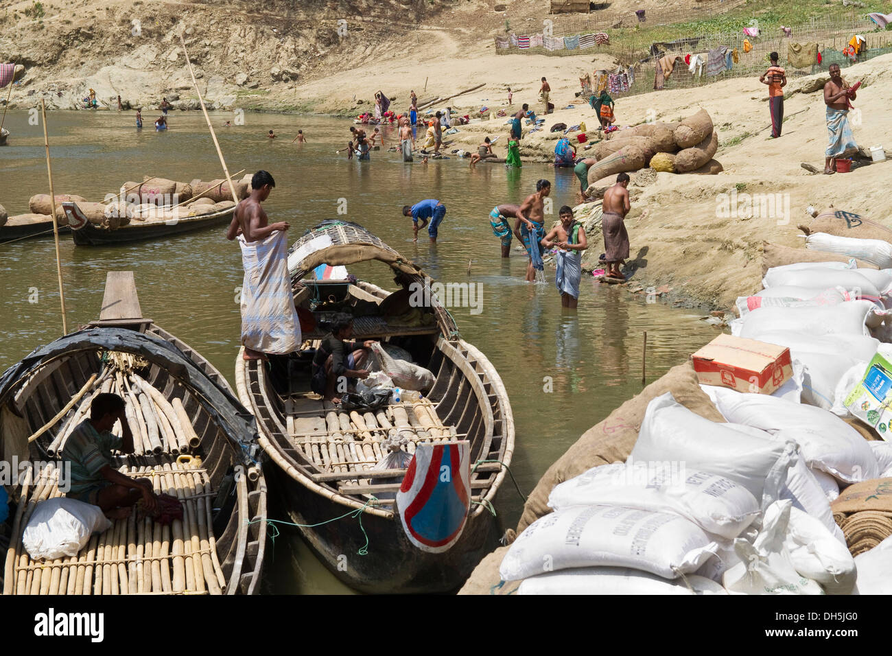 Bustling village life at a jetty, boating drivers resting, villagers washing themselves and their clothes, Ruma Bazar Stock Photo
