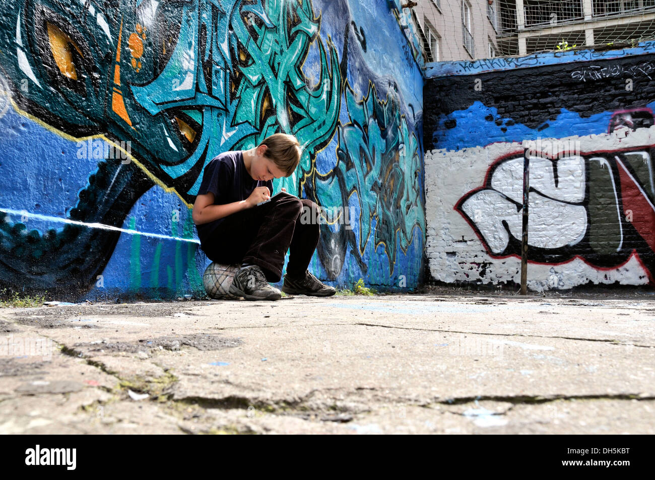 Ten-year-old boy playing with his Nintendo in front of a graffiti wall Stock Photo