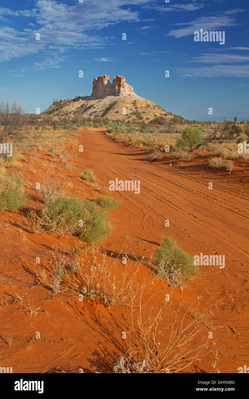 Outback landscape with long red road crossing plains to Castle Rock, unique geological feature in Northern Territory Australia Stock Photo
