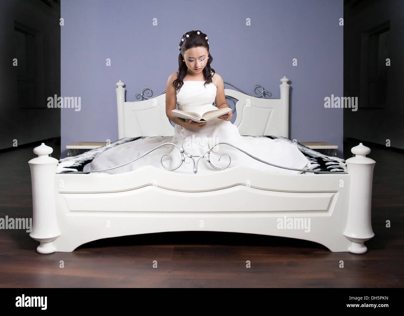 Girl in a long dress on a white bed reads the book Stock Photo