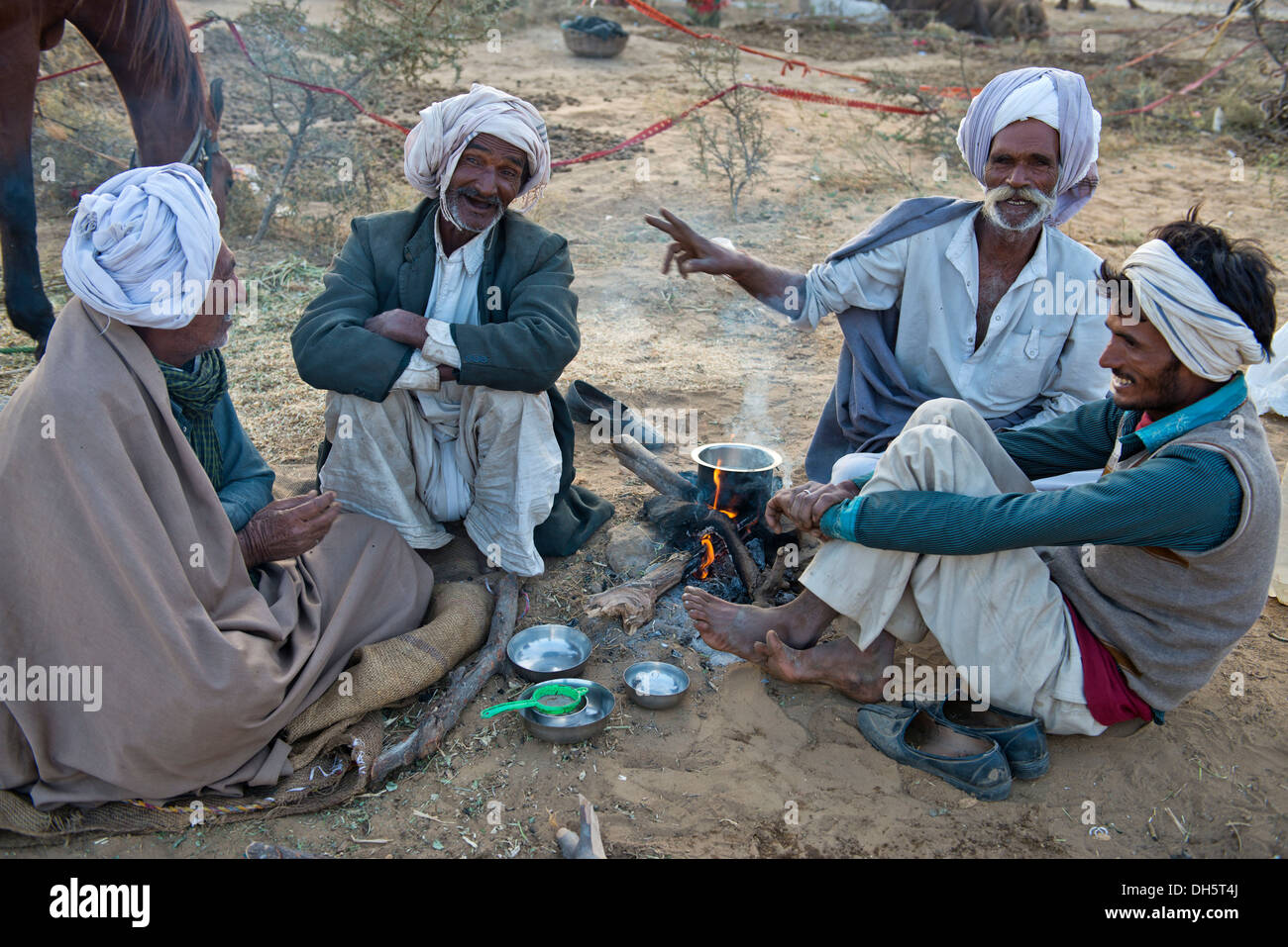 Four Indian men in turbans sitting on the ground having a conversation, milk tea is being prepared over an open fire Stock Photo