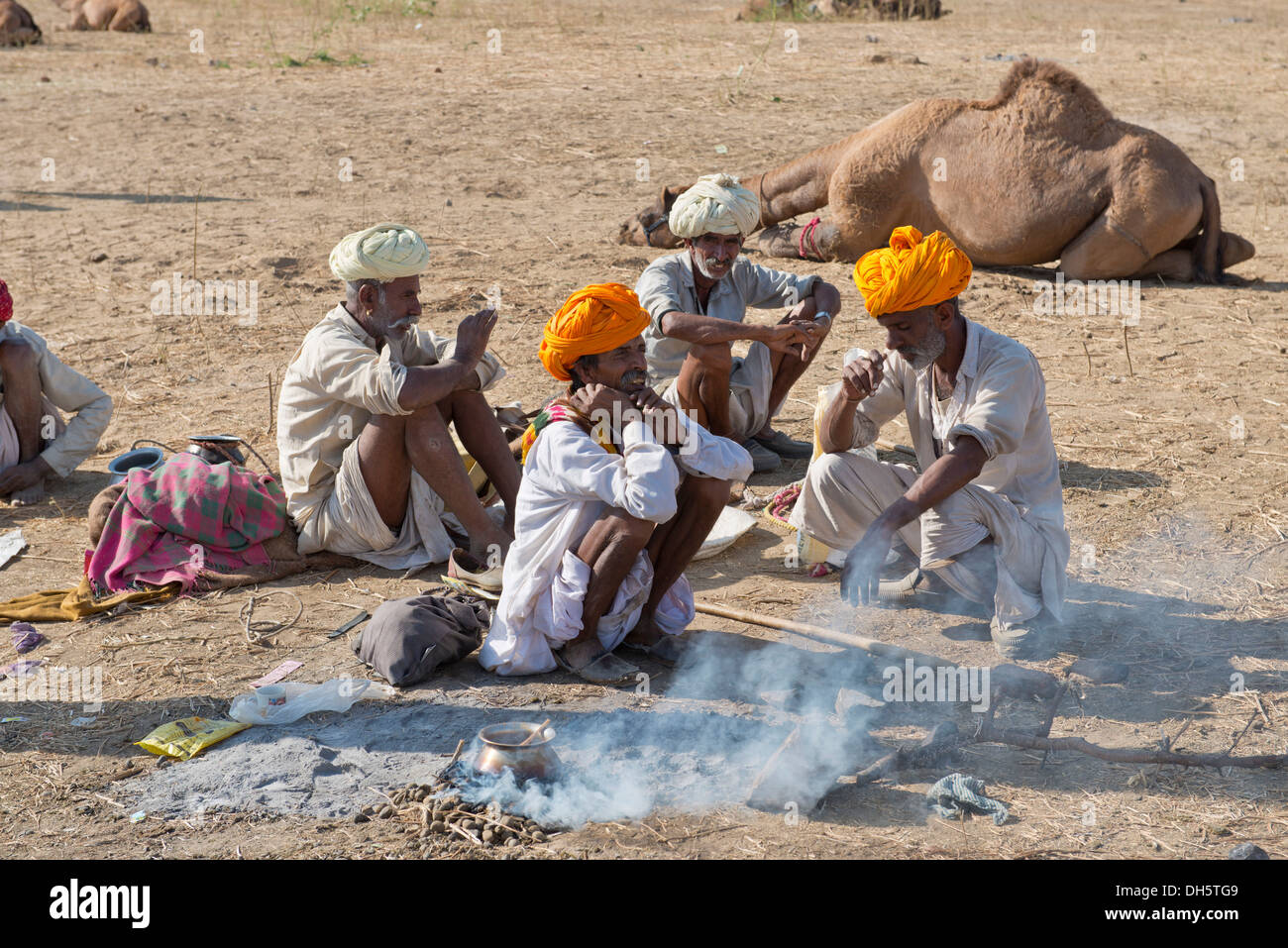 Four elderly Indian men with turbans and wearing the traditional Dhoti garment squatting on the ground, food is being prepared Stock Photo