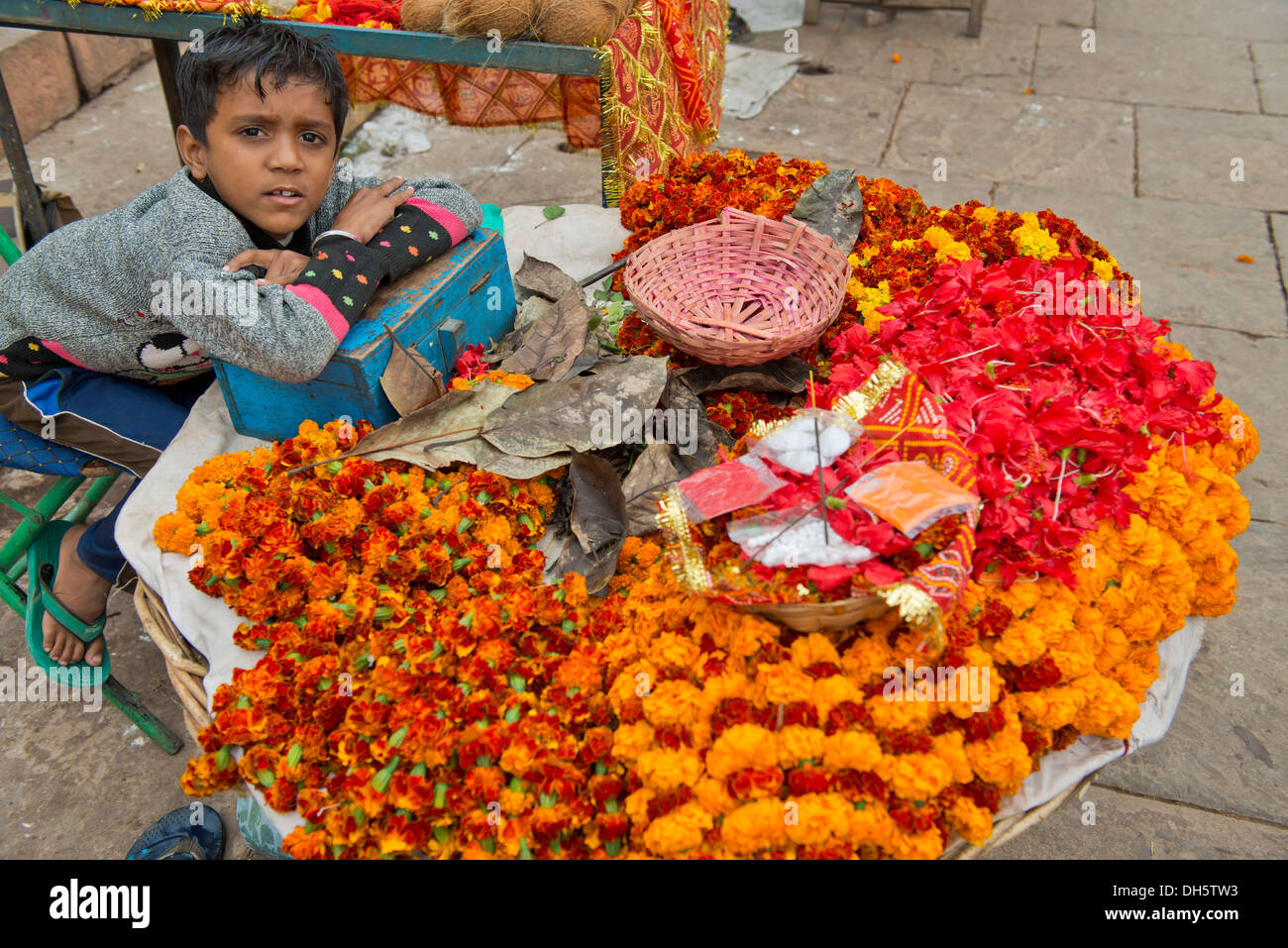 Young boy sitting at a stand for flowers and ritual offerings, the ...
