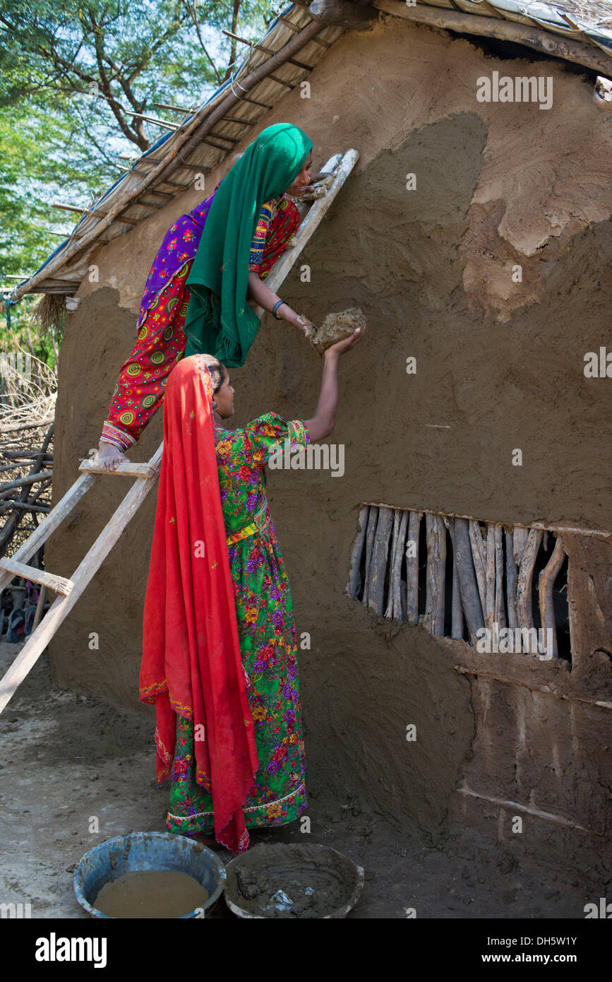 Two women wearing traditional saris rendering a house wall with a mixture of clay, sand and cow dung, Rann of Kutch, Gujarat Stock Photo
