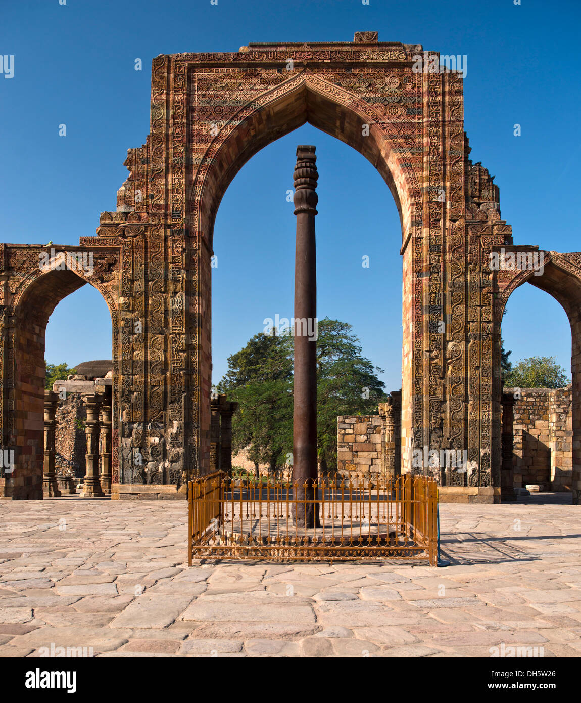 Entrance portal of the Quwwat-ul-Islam Masjid Mosque with relief decorations and an iron pillar in the courtyard, Qutb Minar Stock Photo
